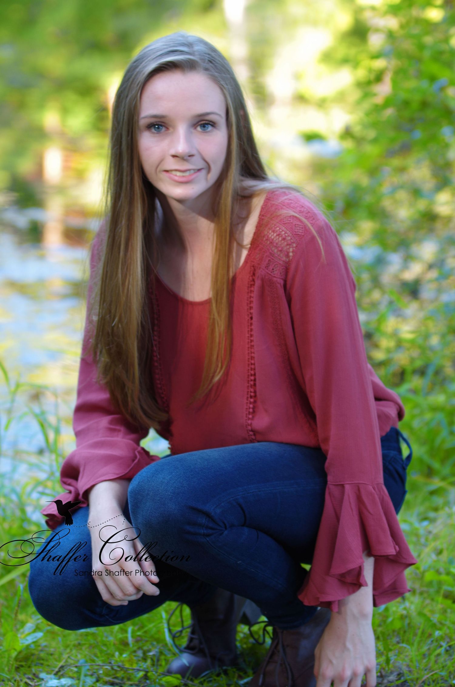 Casual outdoor portrait in burgundy top amid green foliage.