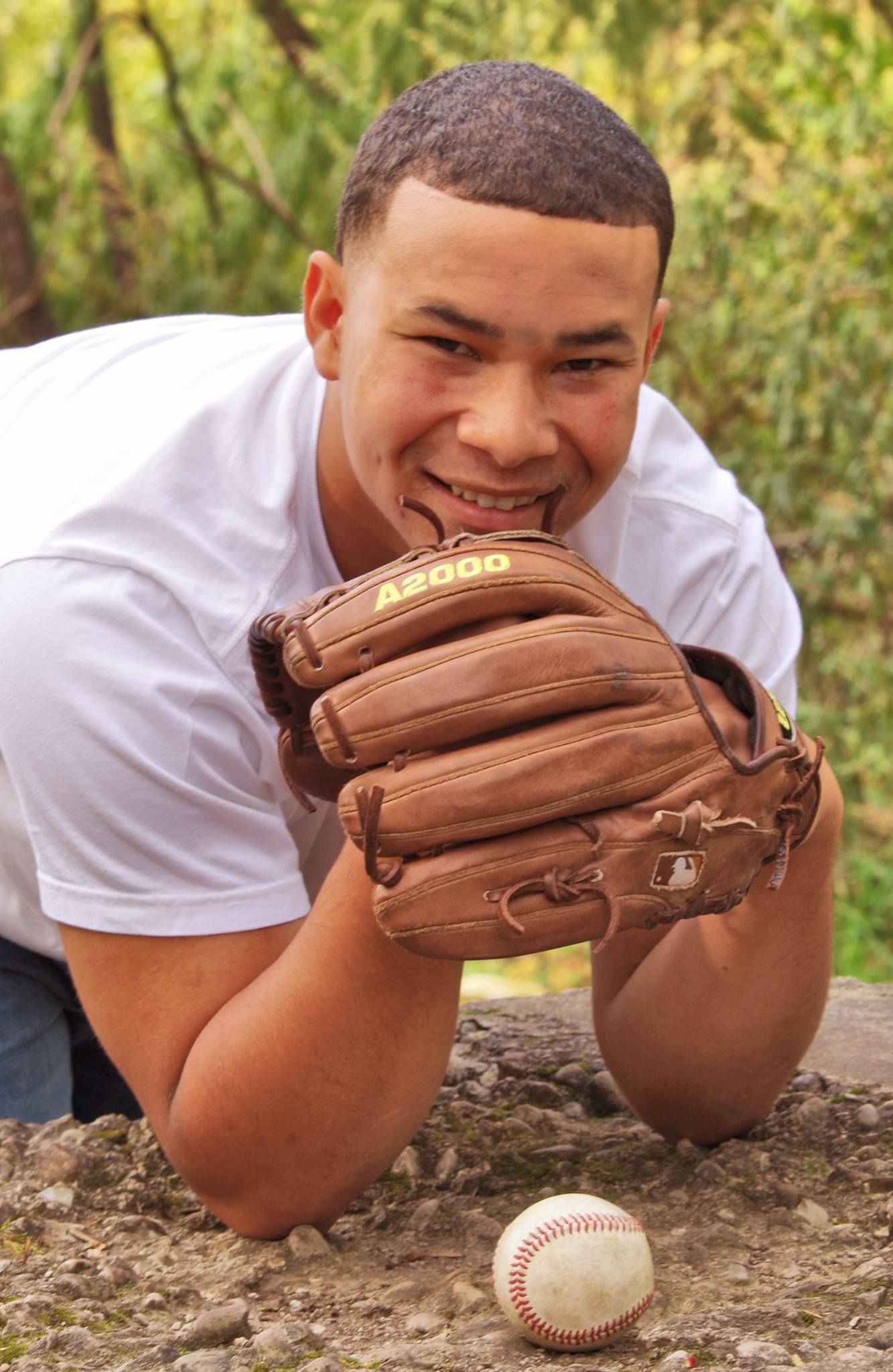 Baseball player lying down with glove and baseball on stone surface outdoors.