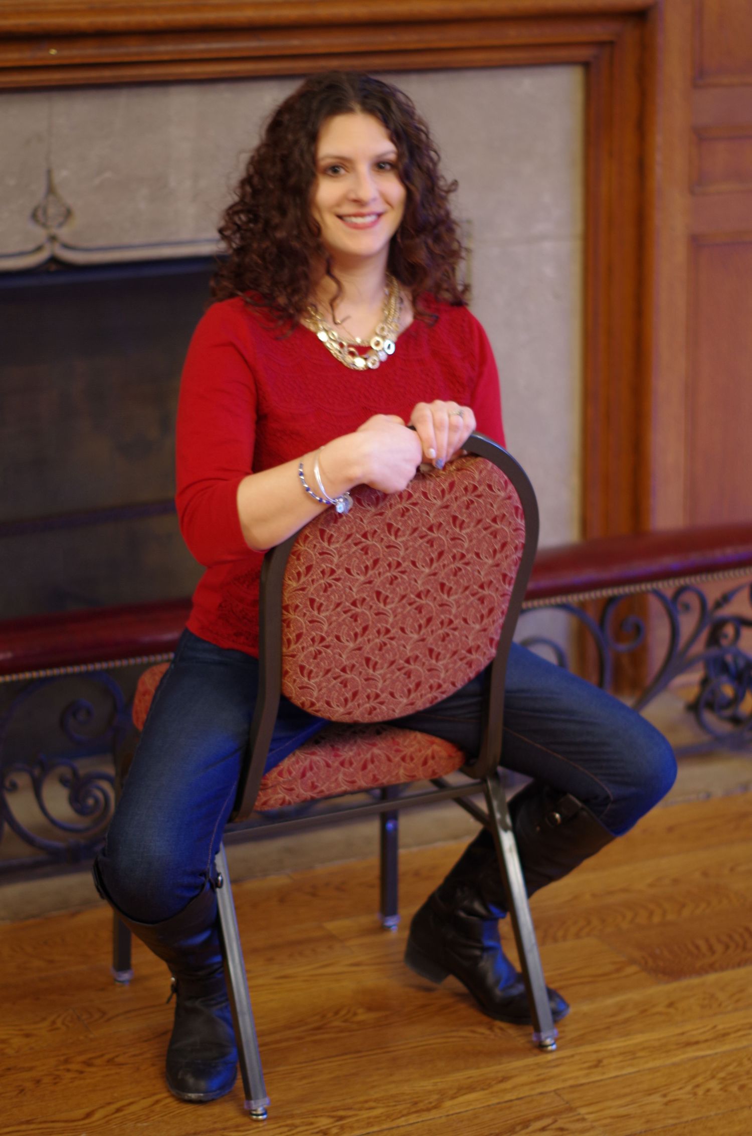 A person in a red sweater sits casually on a patterned chair indoors.