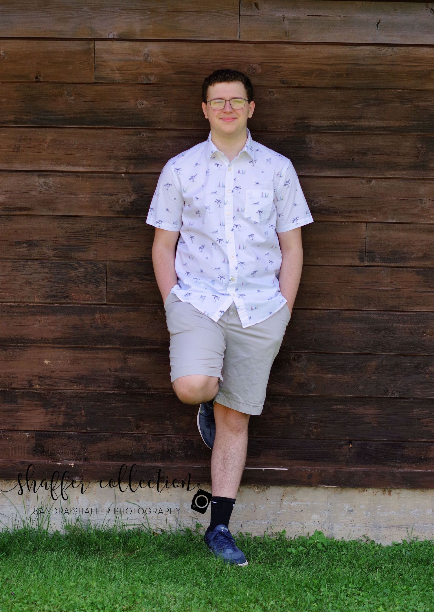 Casual summer portraits against rustic wooden wall wearing patterned shirt and shorts.