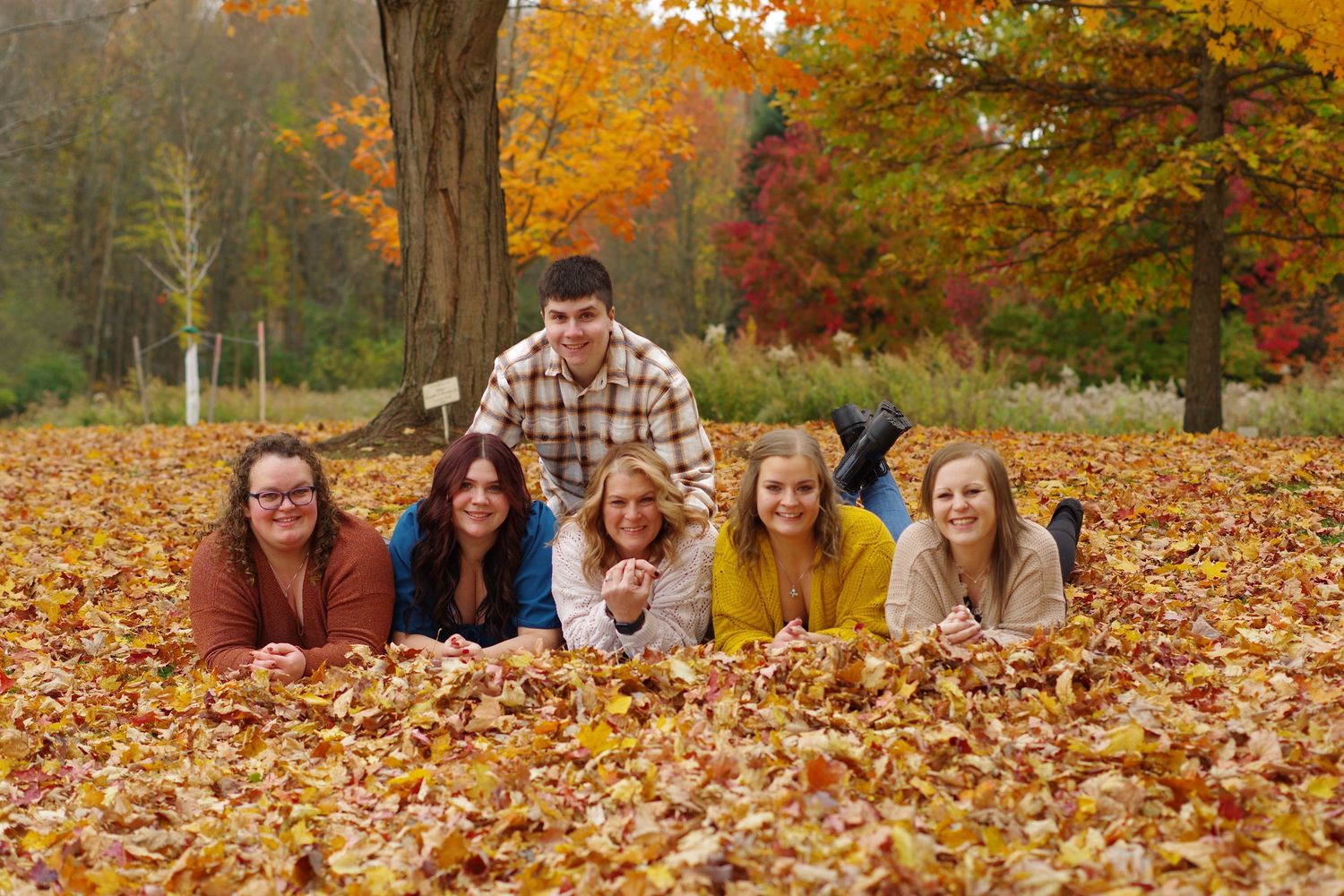 Group posed lying in colorful fallen autumn leaves during outdoor photo shoot.