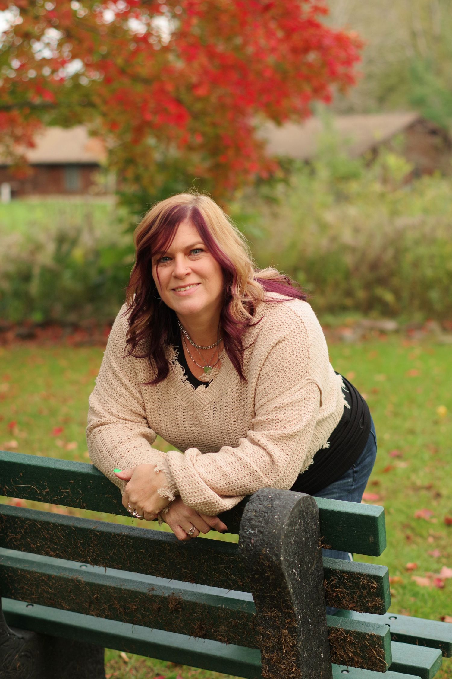 Casual autumn portrait on park bench with cozy sweater and fall foliage in background.