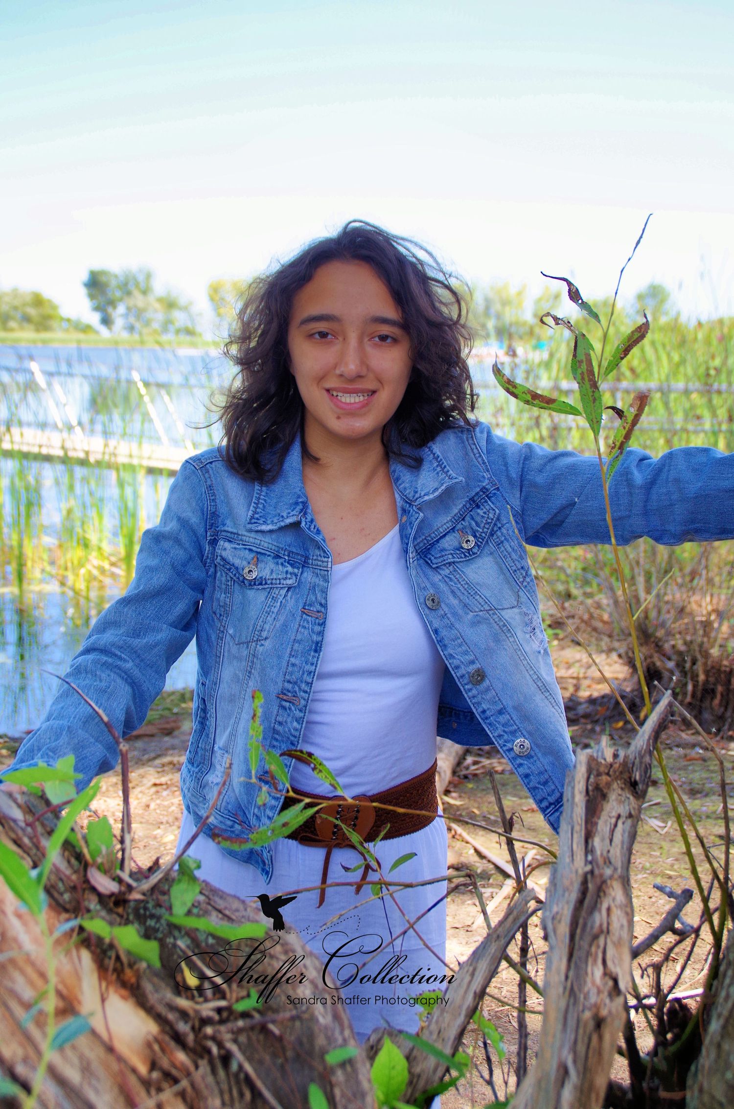 Casual outdoor photoshoot in denim jacket by the water with natural lighting and plants.