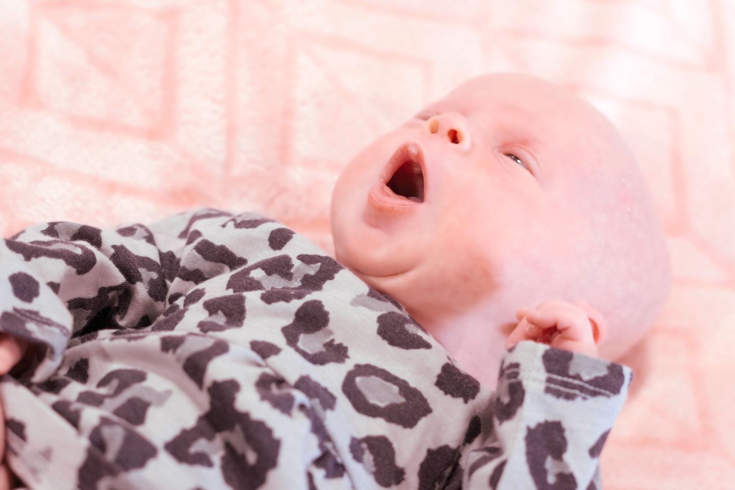 Baby in leopard print outfit laughing against pink background.