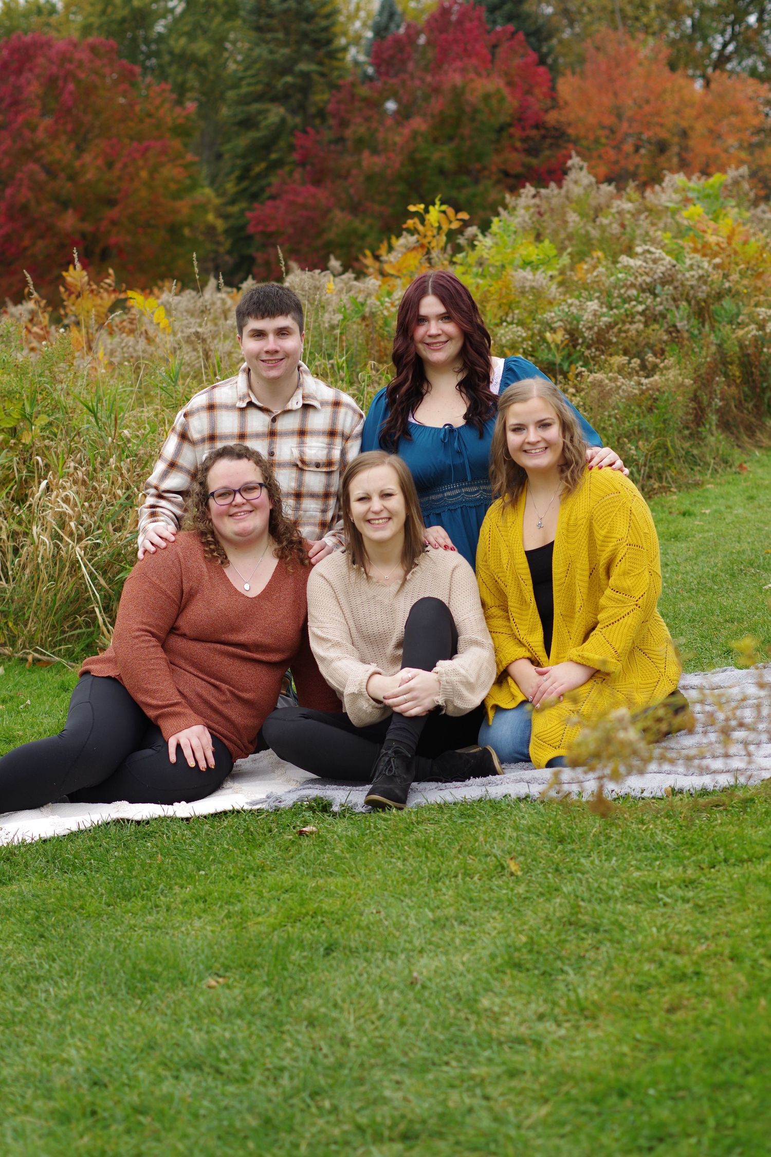 Family group seated on grass with colorful fall trees and wildflowers in background.