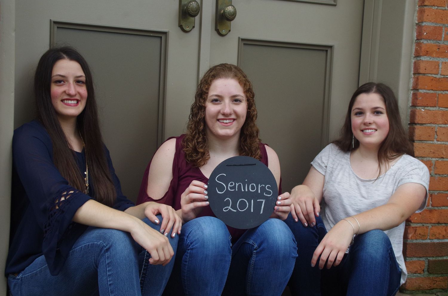 Three students pose together on steps holding Seniors 2017 sign.