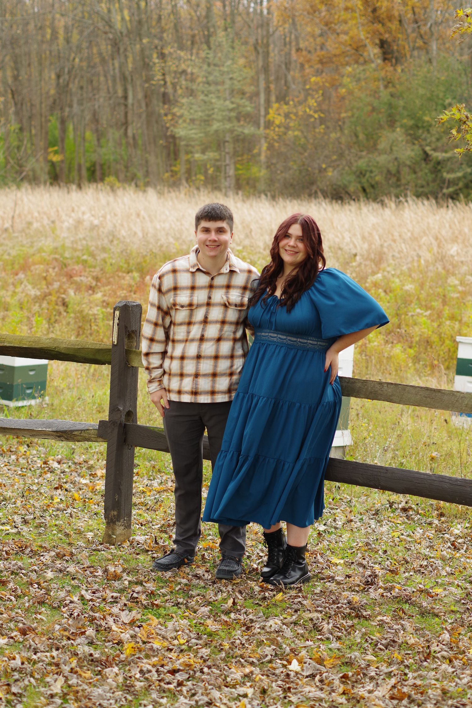 Couple posing by rustic fence surrounded by fall foliage and meadow grasses.