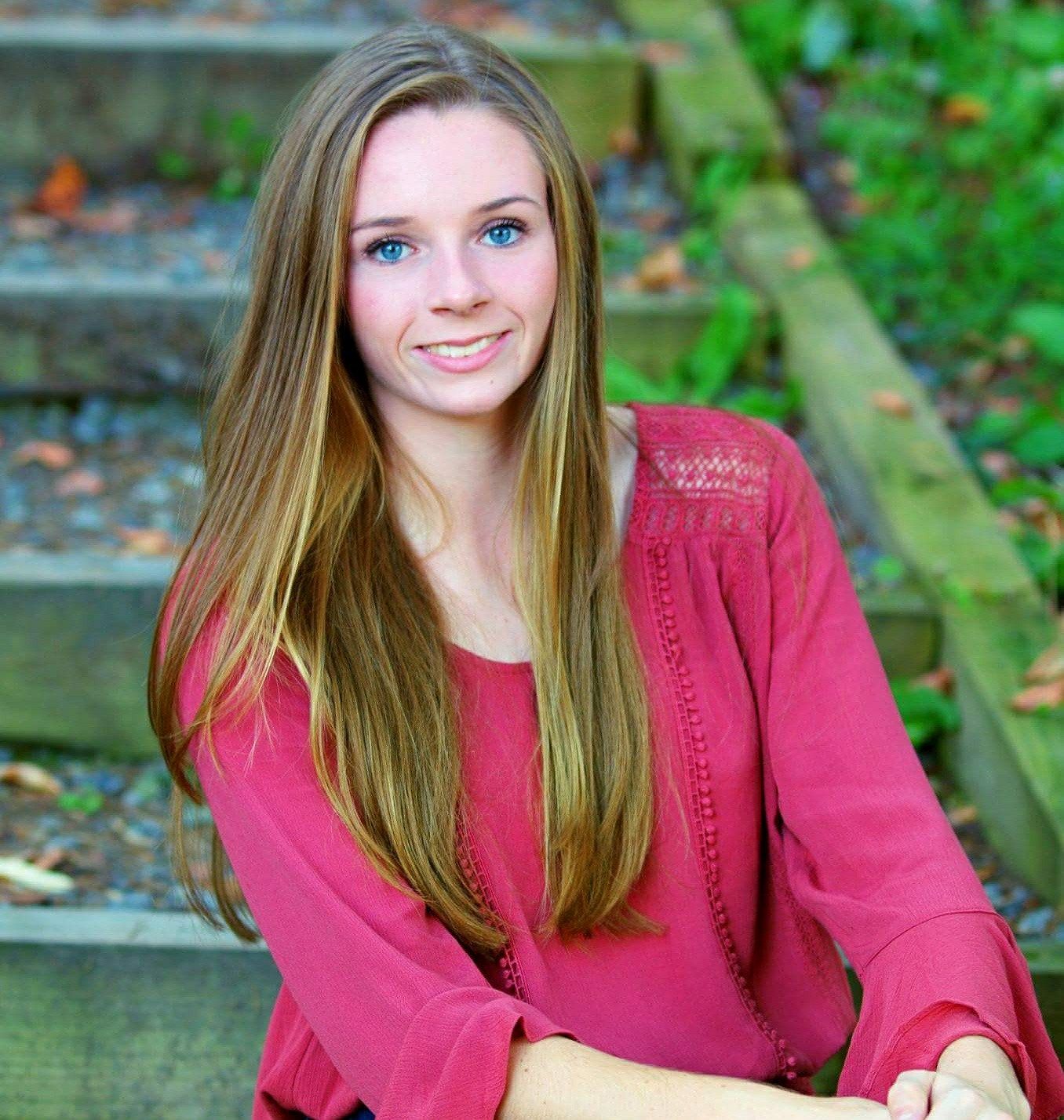 Outdoor portrait on wooden steps wearing a bright red sweater against natural backdrop.