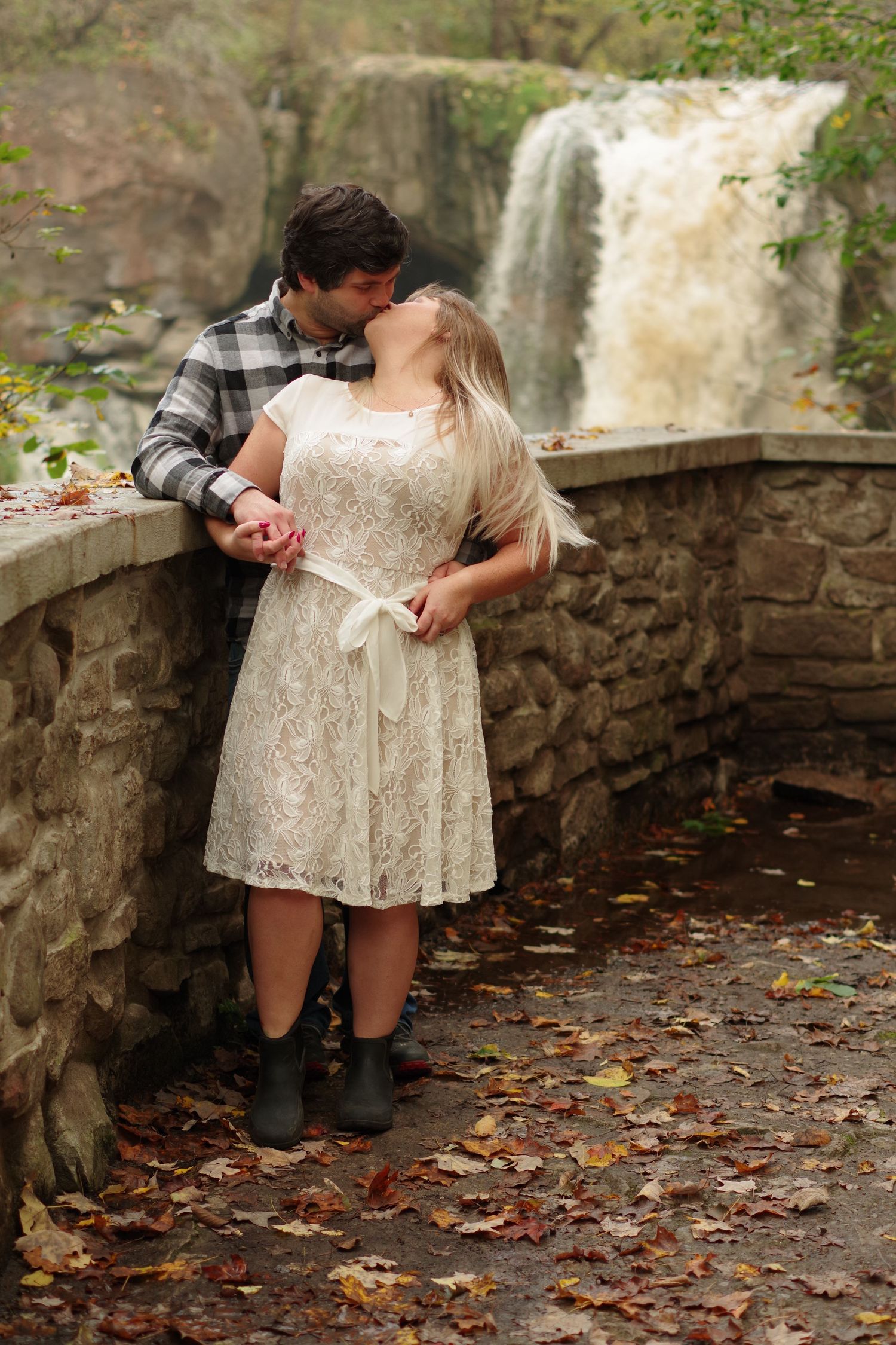 Couple posing playfully by stone wall with waterfall in background.