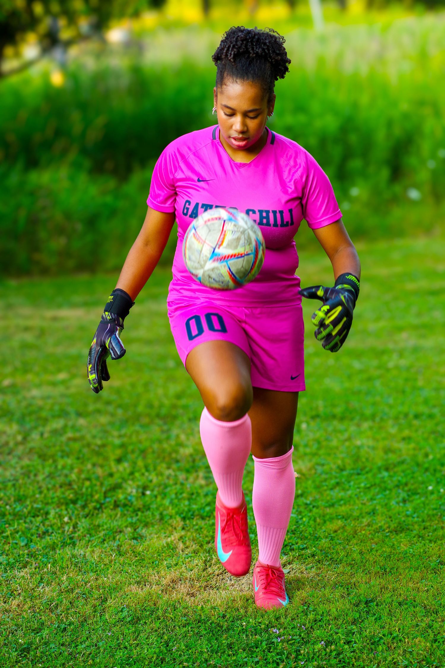 A soccer goalkeeper in bright pink uniform and gloves practices diving saves on a green grass field in dynamic motion.