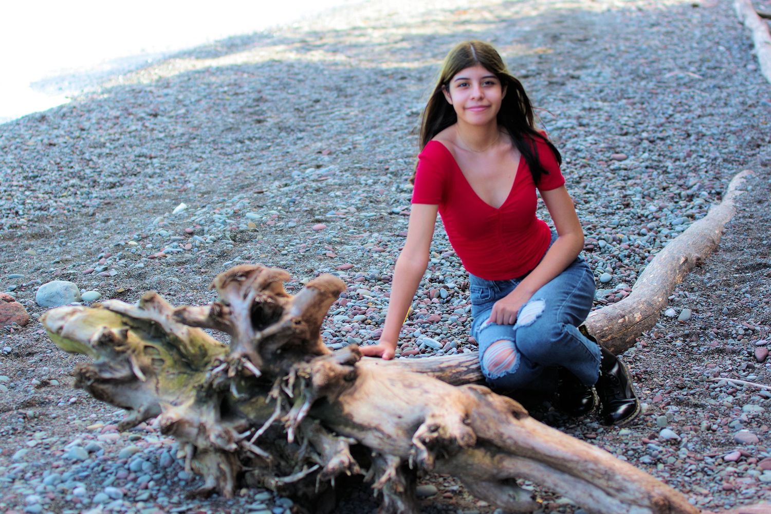 Casual portrait by beach driftwood wearing red v-neck top and blue jeans.