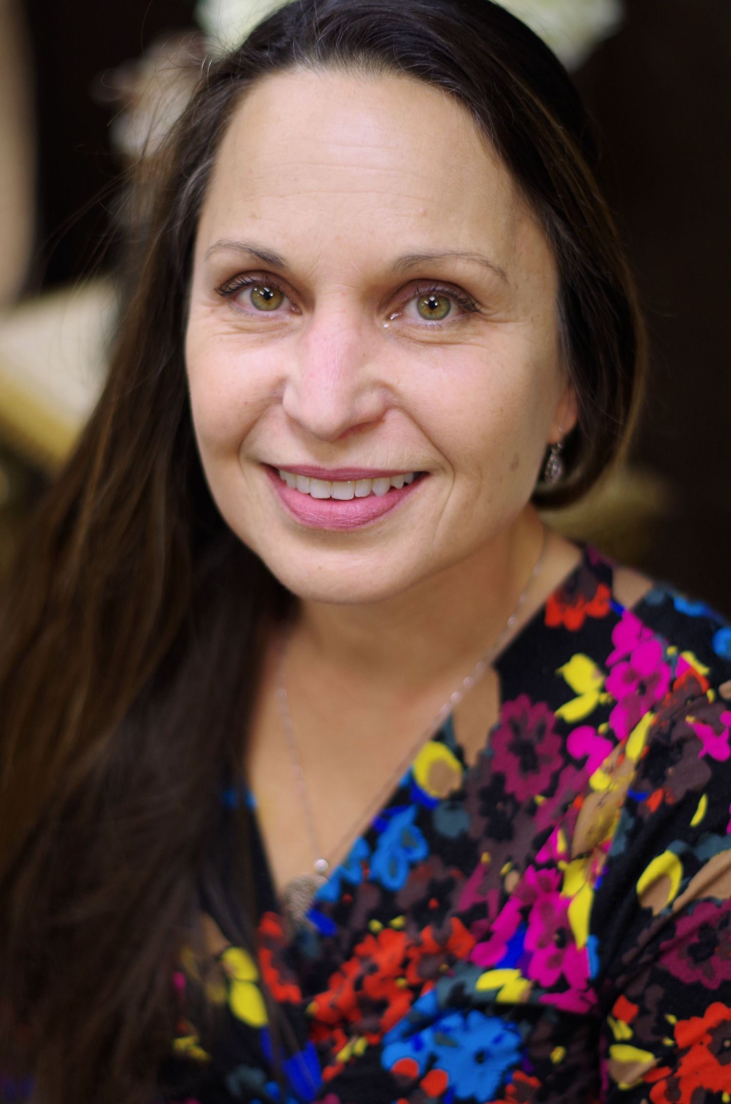 Professional portrait showing a smiling woman with long dark hair wearing a colorful floral patterned dress.