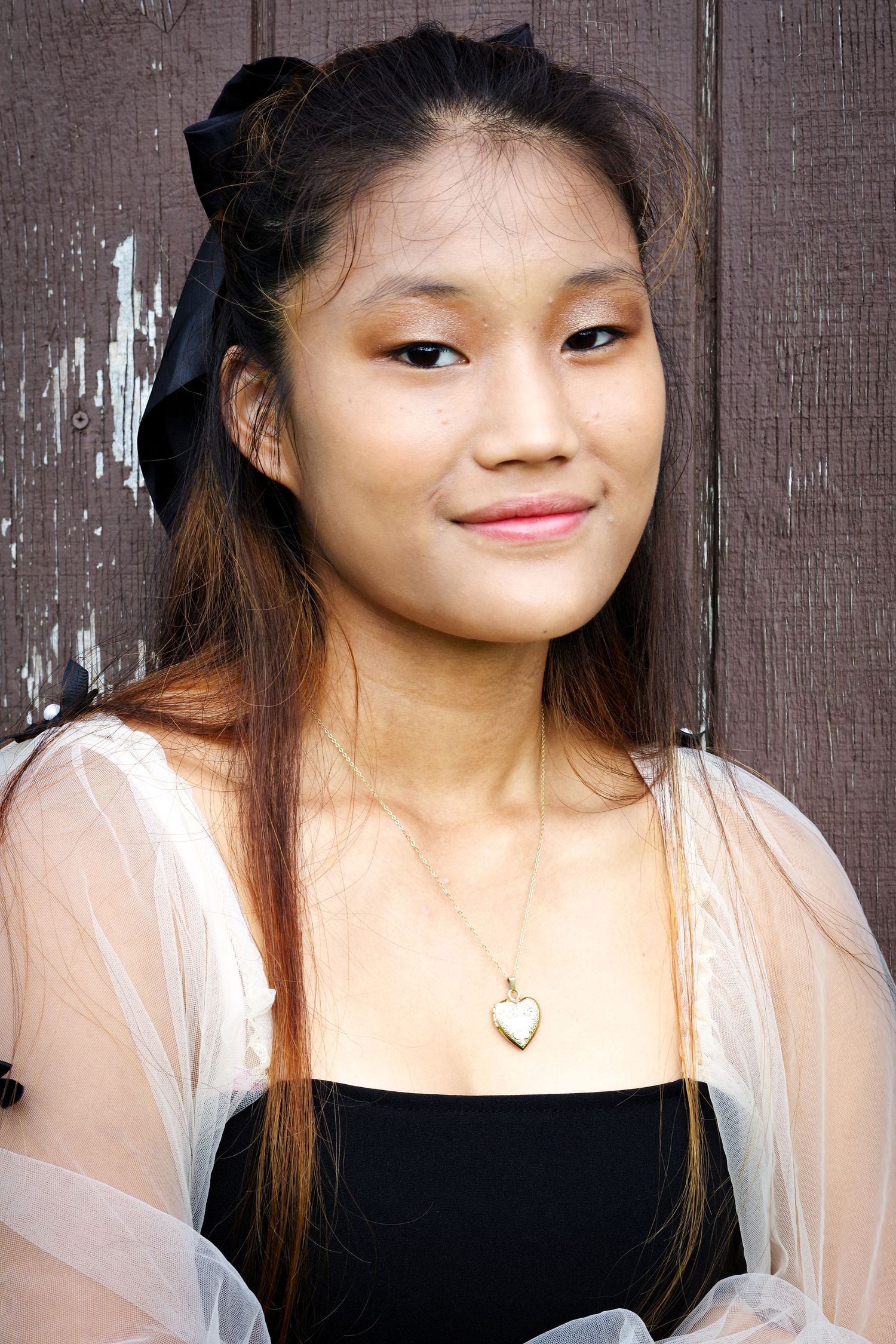 Close-up portrait against wooden background wearing sheer top and heart necklace.