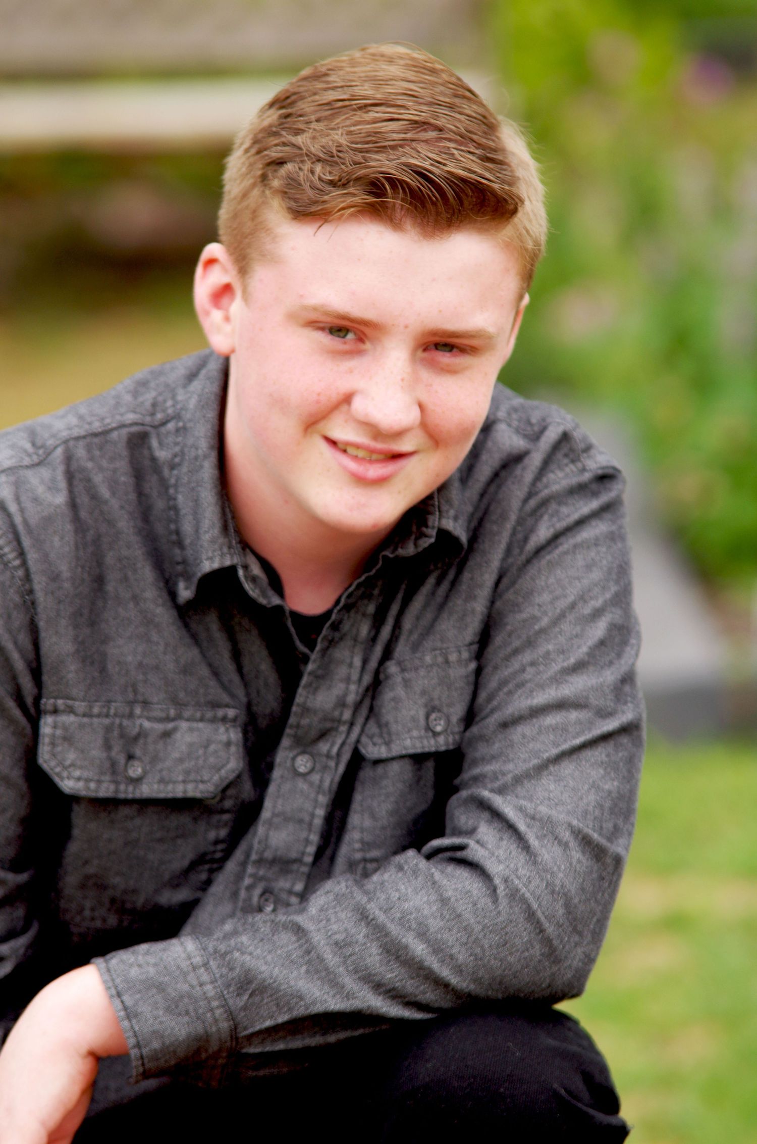 Casual portrait in gray button-down shirt against natural outdoor background.