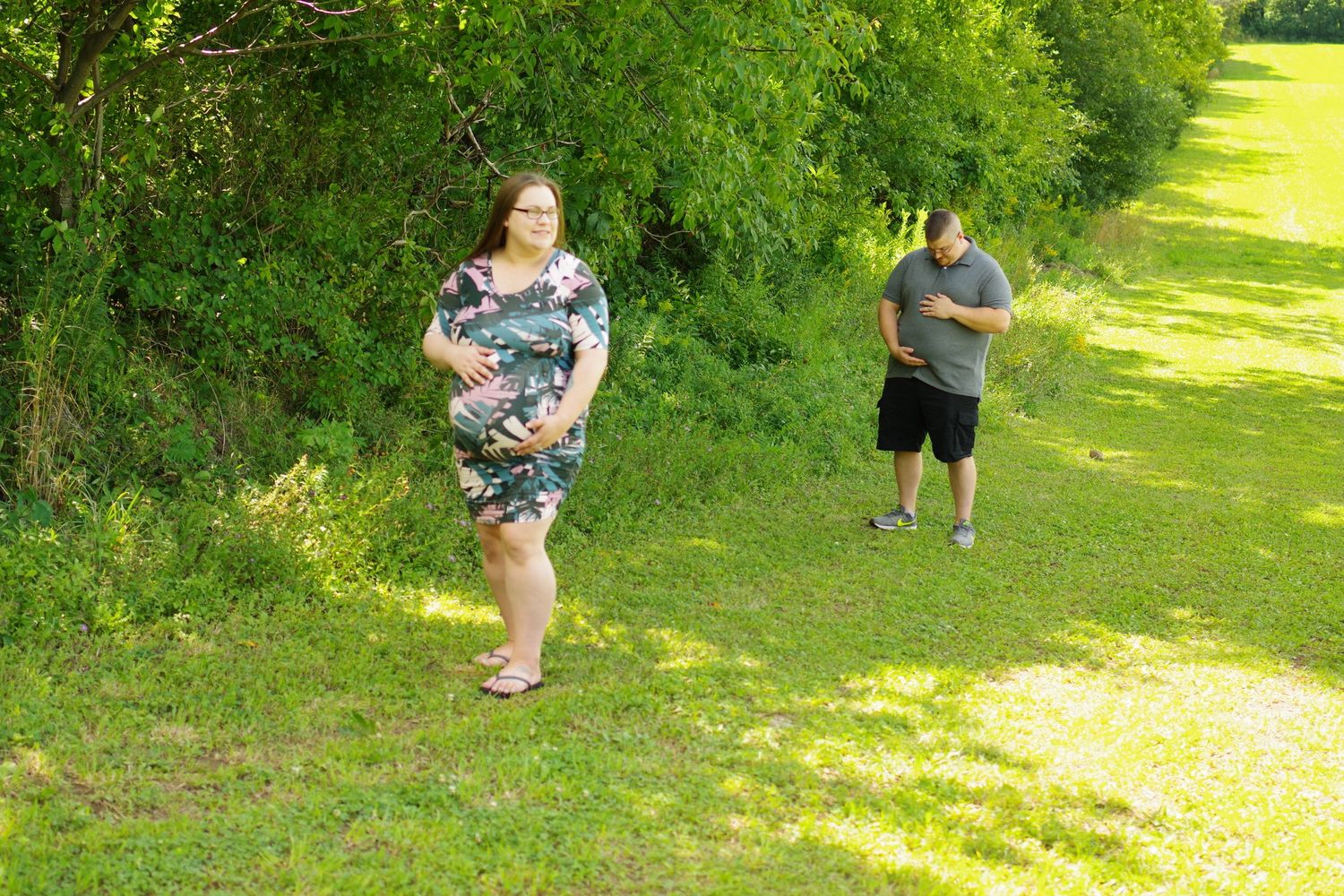 Playful outdoor maternity photoshoot in green summer setting.