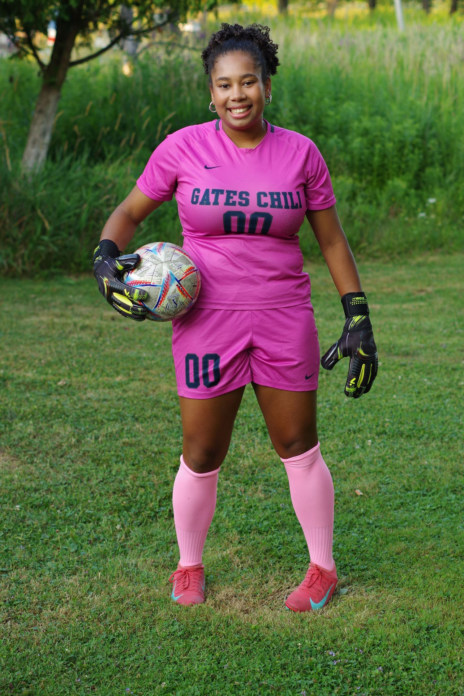 Soccer player in pink Gates Chili uniform holding ball with goalkeeper gloves and pink socks.