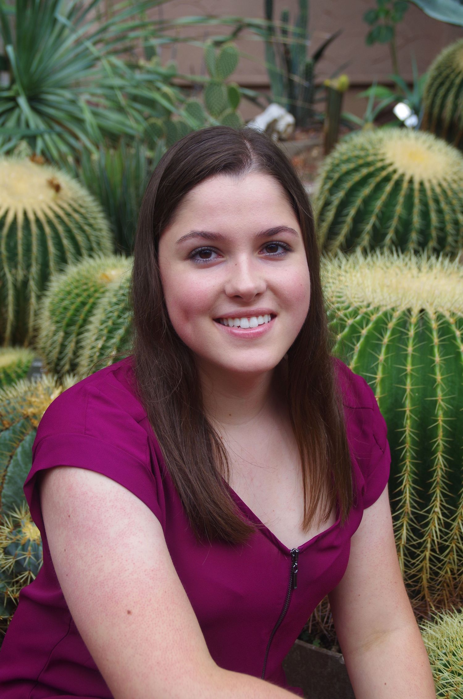 Person in burgundy top poses near barrel cactus in desert garden setting.