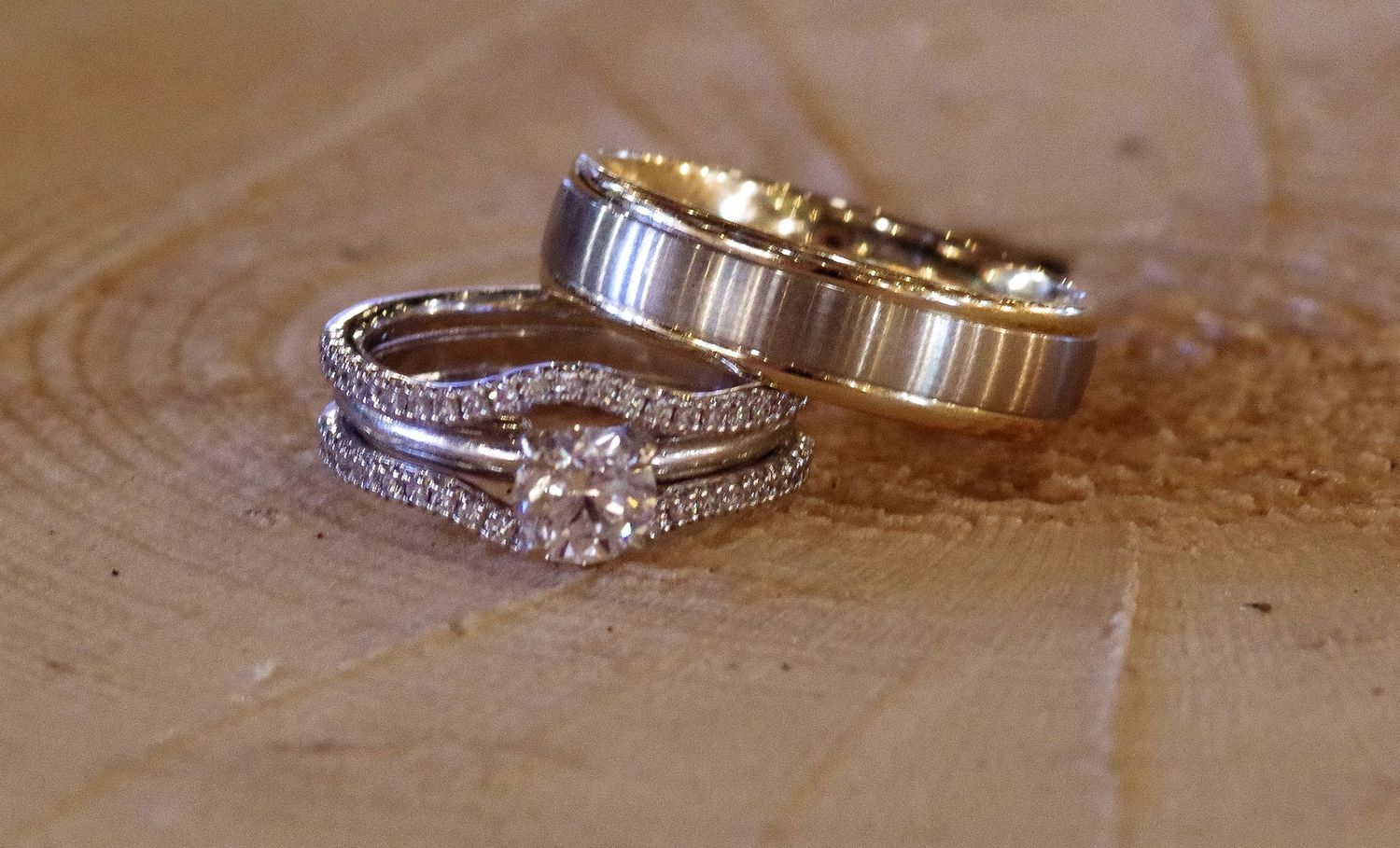 Two elegant wedding rings, a diamond-studded white gold band and a brushed yellow gold band, resting on a wooden surface.