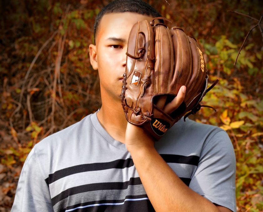 Young baseball player holding a Wilson leather mitt up to his face outdoors.