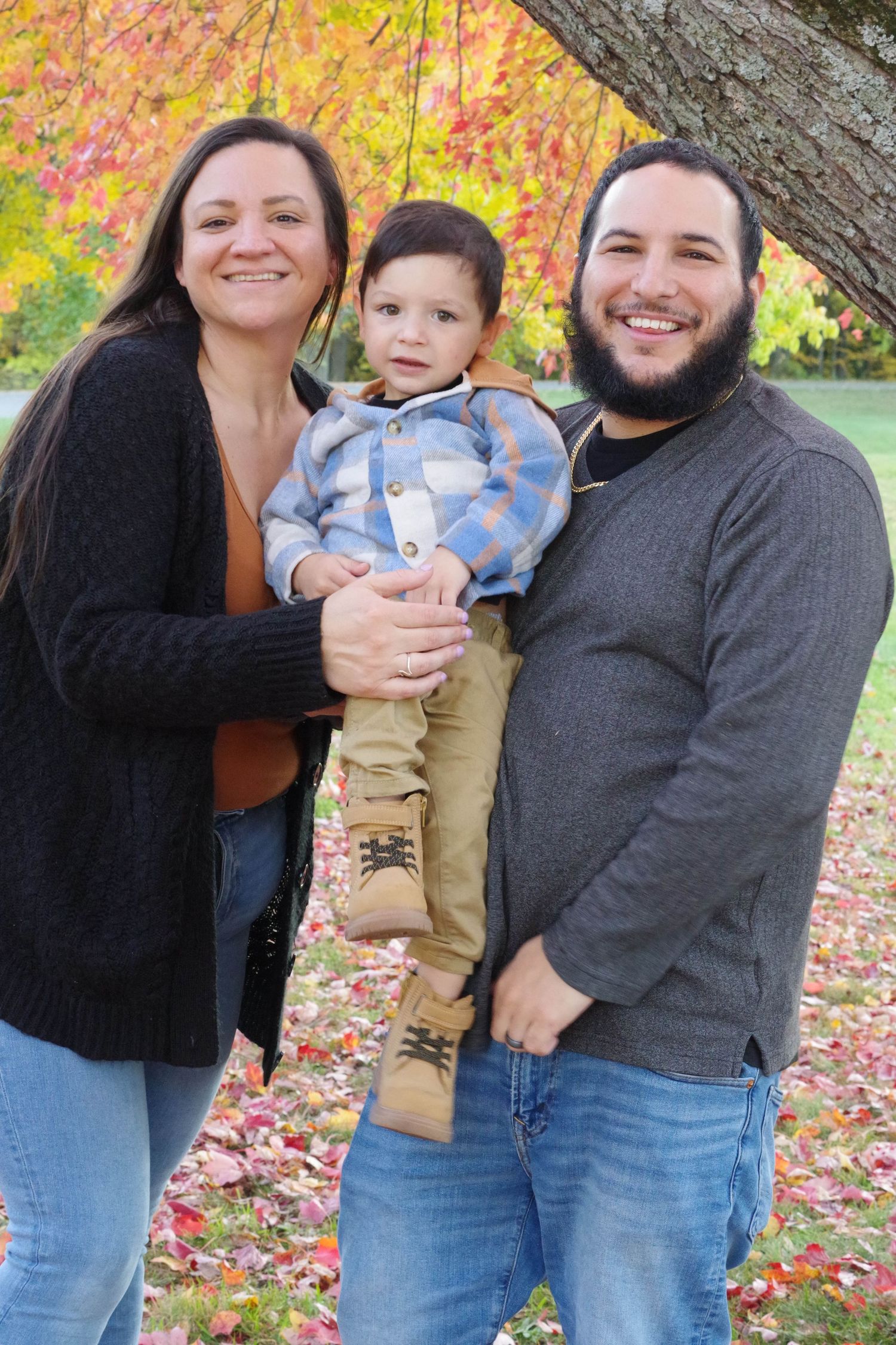 Family poses together outdoors with fall foliage and trees in background.