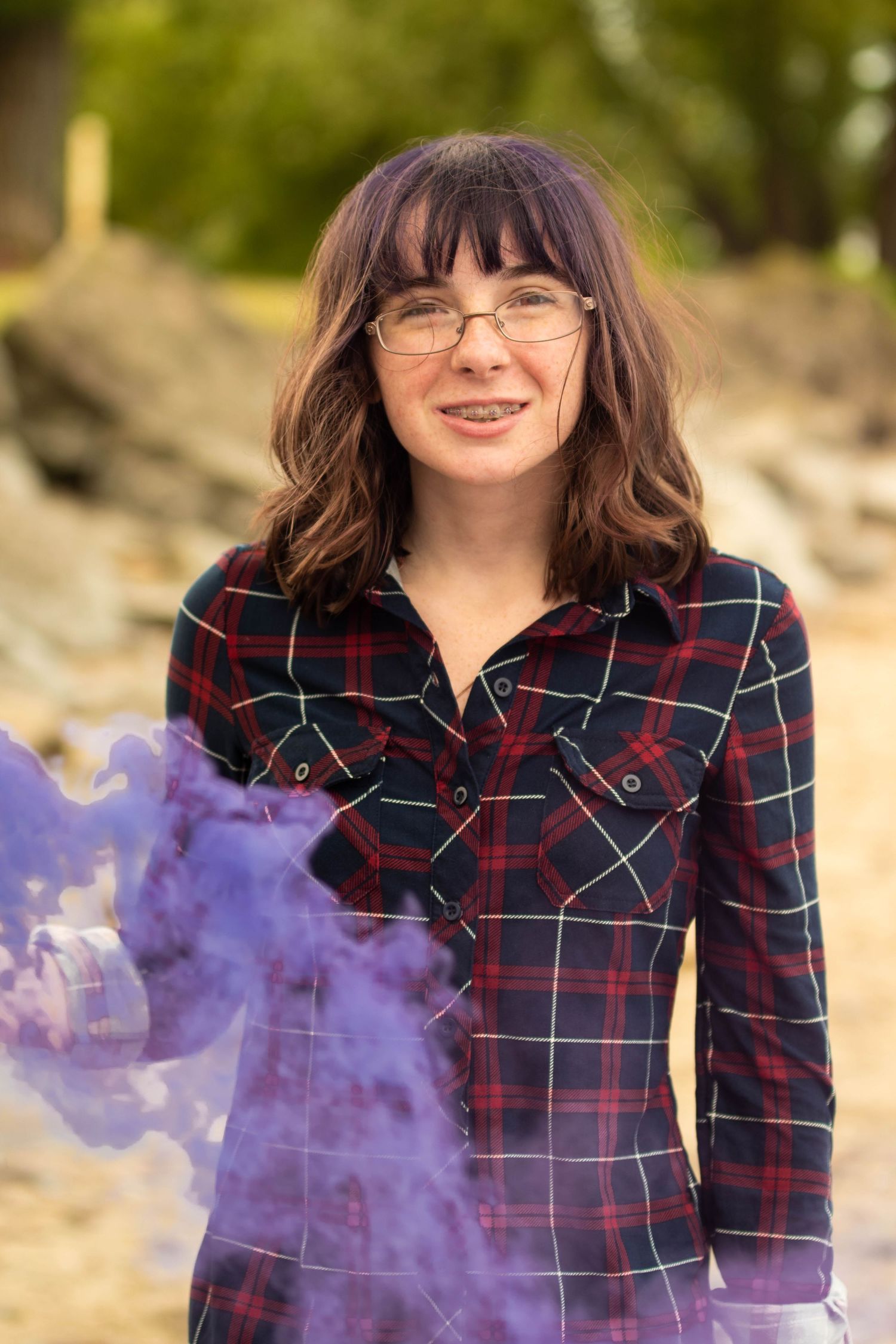 Person with purple smoke effects in outdoor photo session wearing plaid shirt.