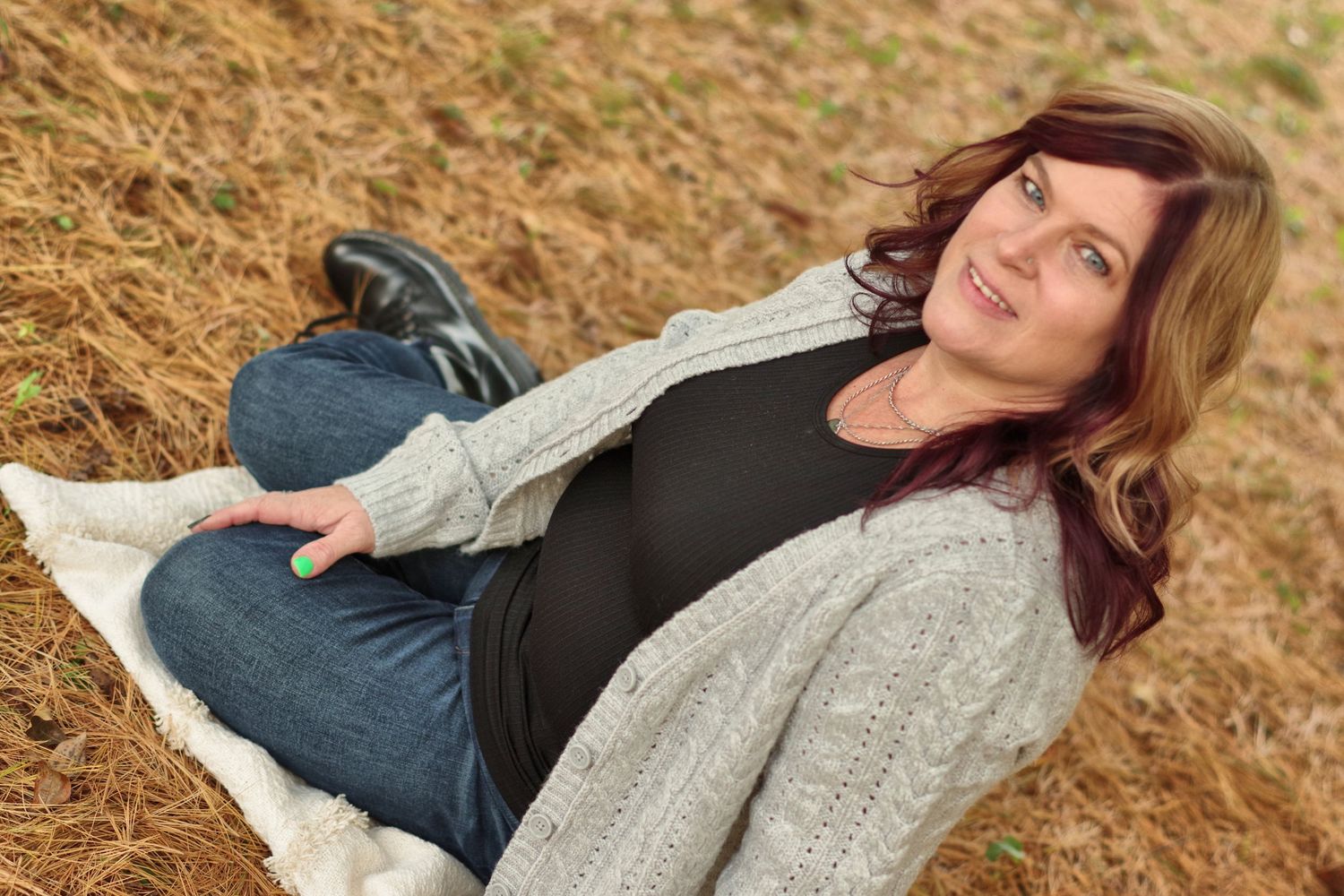 Person relaxes on blanket wearing cozy sweater and jeans in autumn setting.