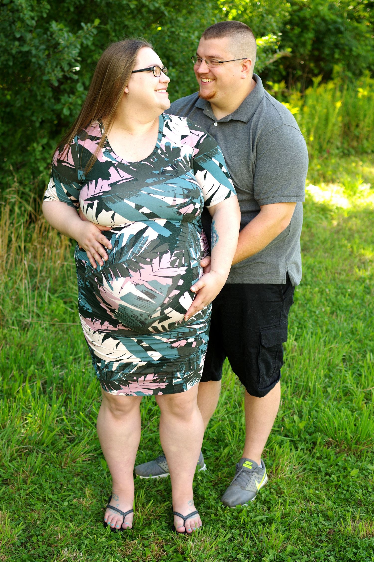 A couple poses together outdoors on green grass wearing casual summer attire.
