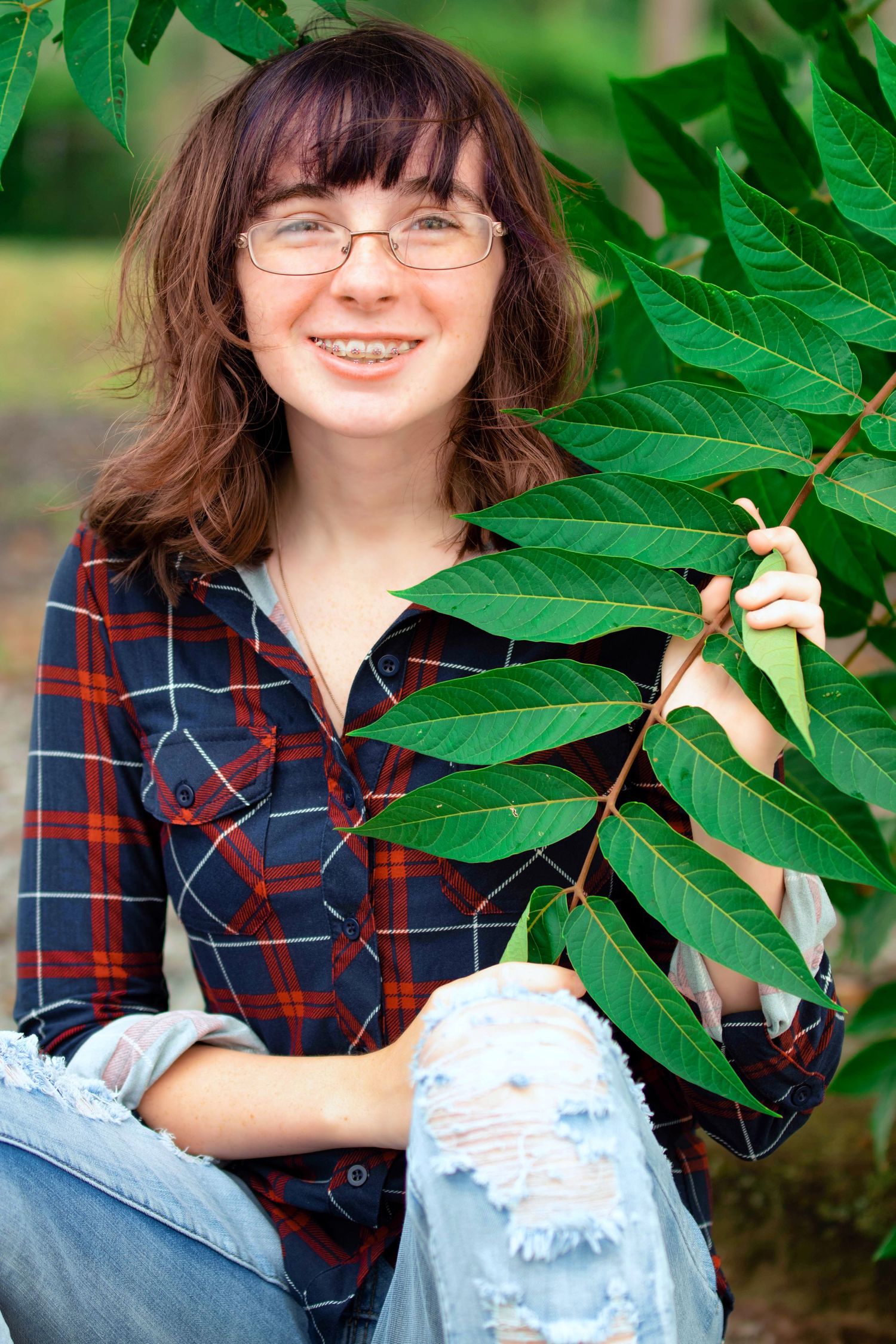 Portrait among green leaves wearing plaid shirt and distressed denim.
