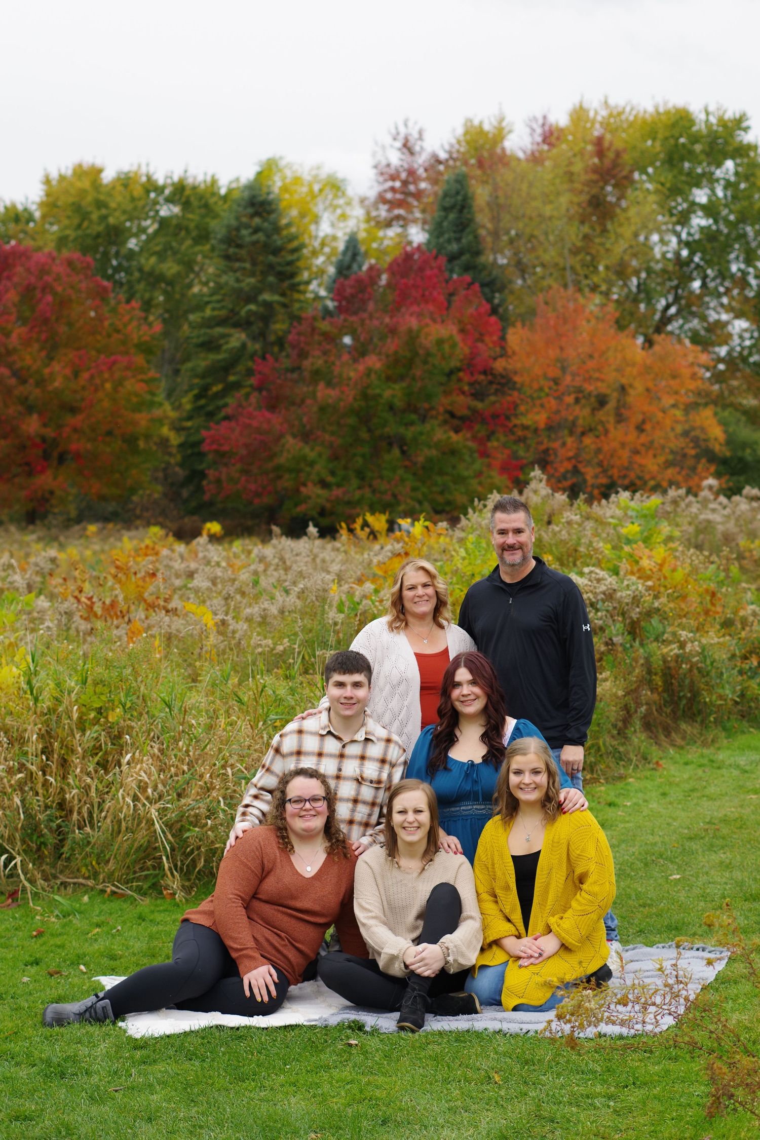 Group portrait against vibrant autumn foliage with red and orange trees in background.