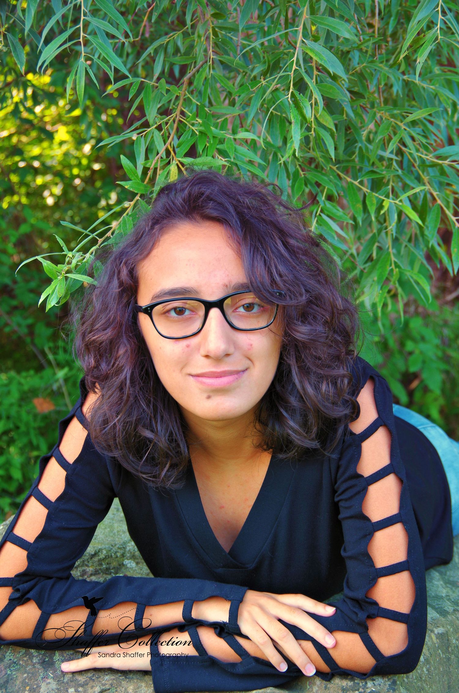 Creative portrait poses against green foliage wearing a dark outfit and glasses.