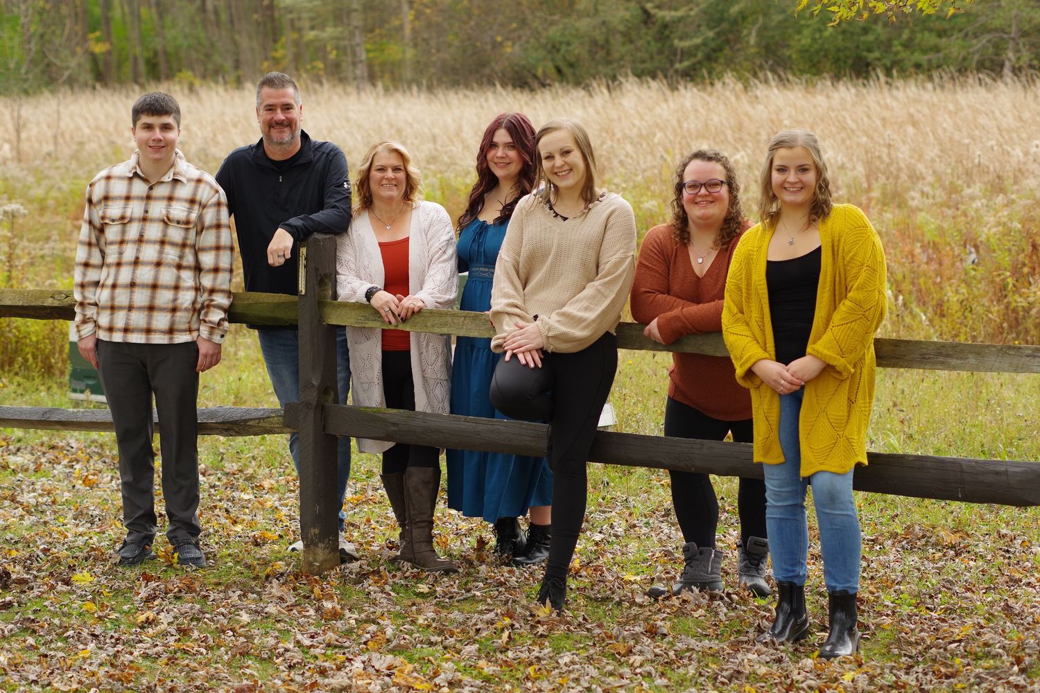 A panoramic display of people sitting on wooden fences in a rural autumn field setting with warm golden tones.