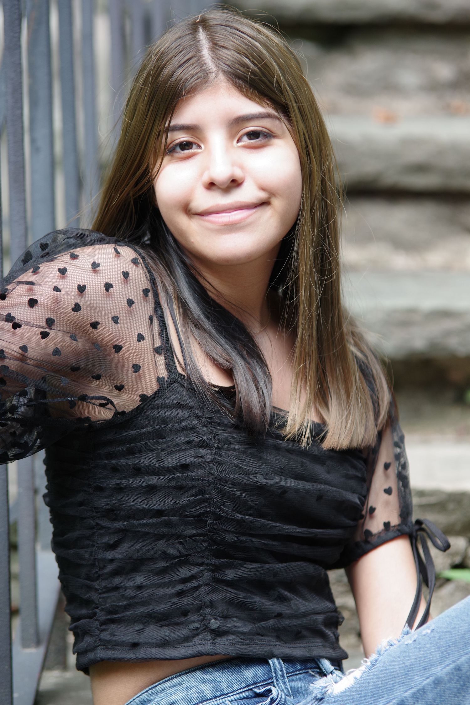 Portrait on stone steps wearing sheer black polka dot top and distressed jeans.