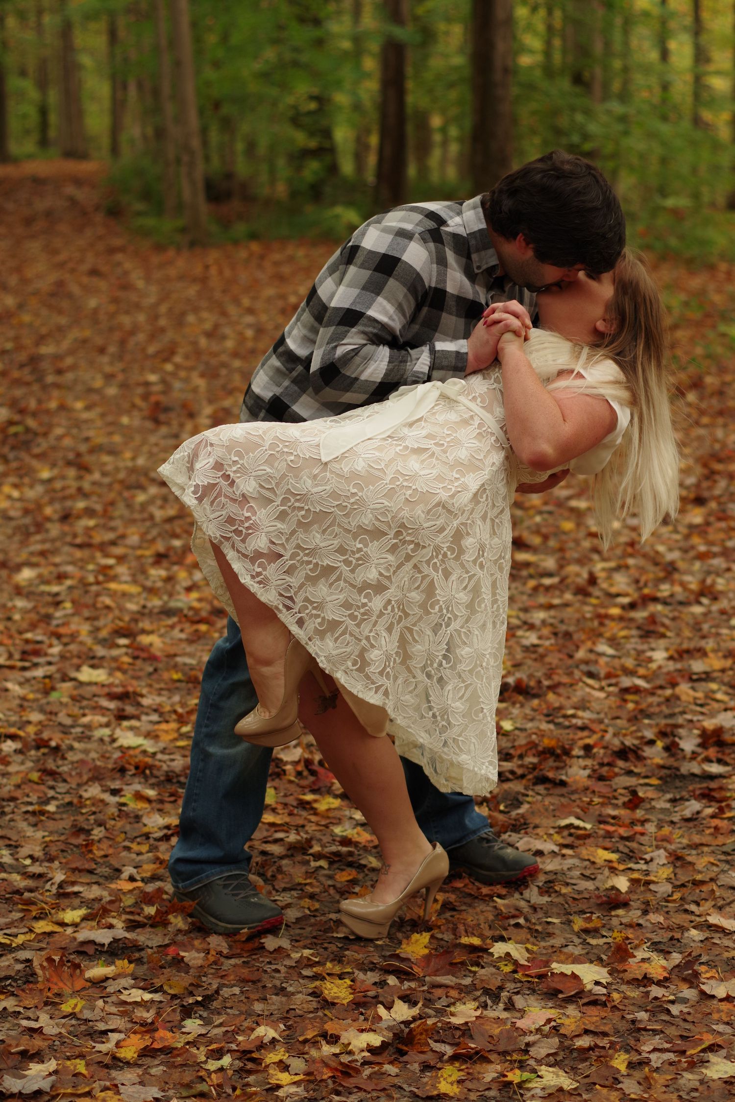 Couple sharing playful kiss in autumn forest with fallen leaves.