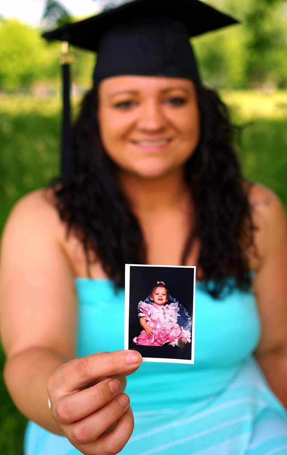Graduate in turquoise dress holds small vintage photographs during outdoor photo session.