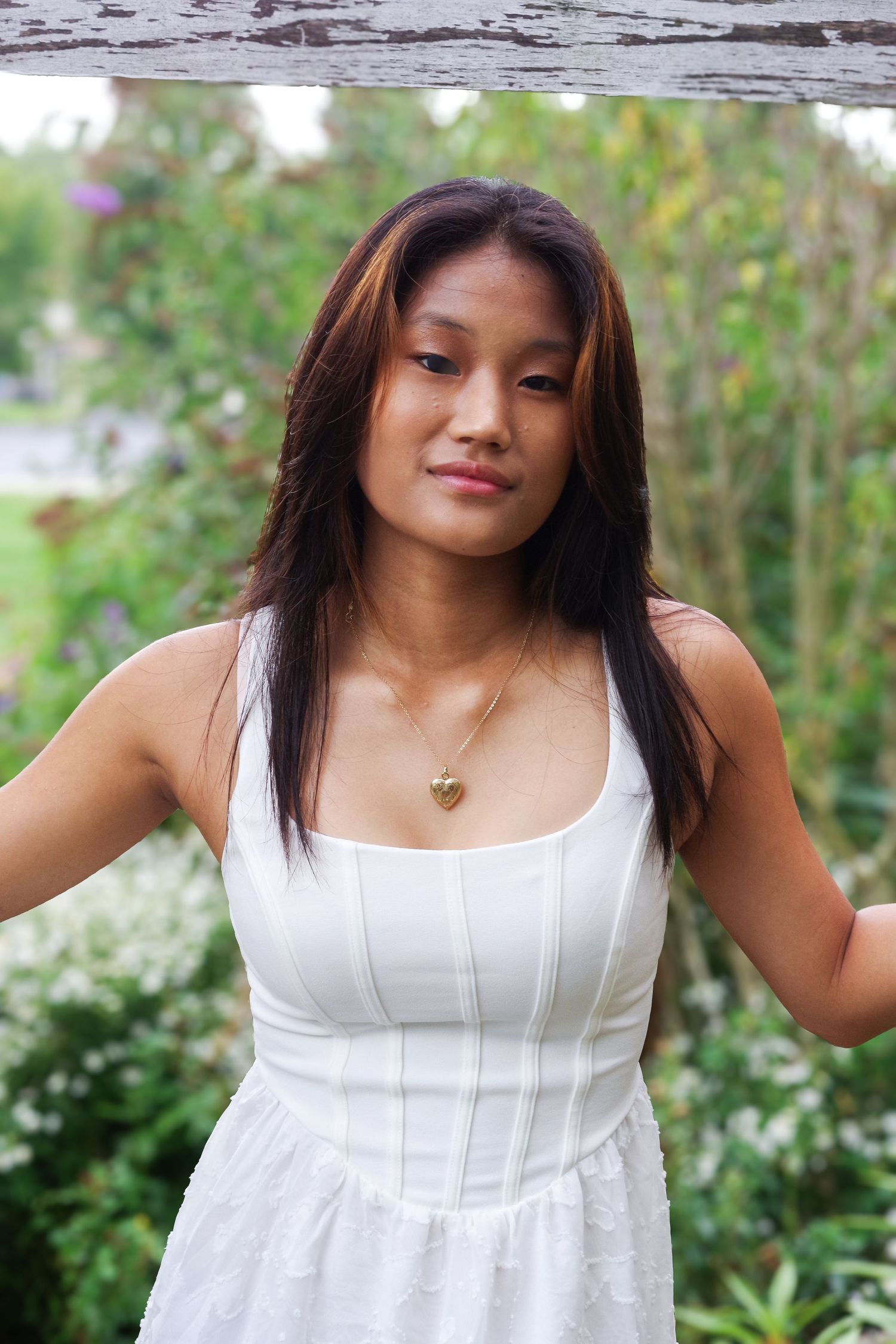 Person in white dress poses against blurred garden background.