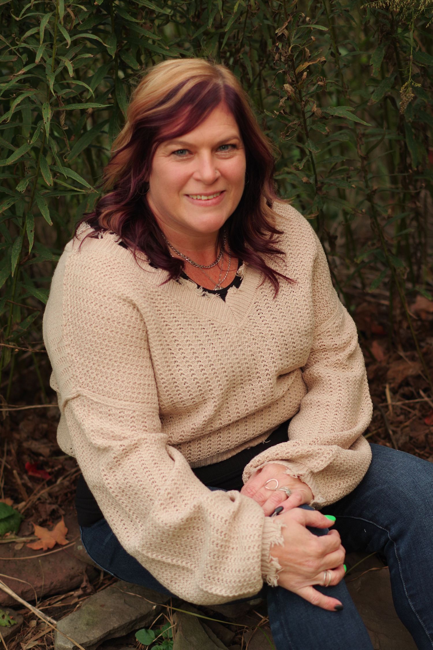 Relaxed outdoor portrait with person wearing cream sweater against natural foliage background.