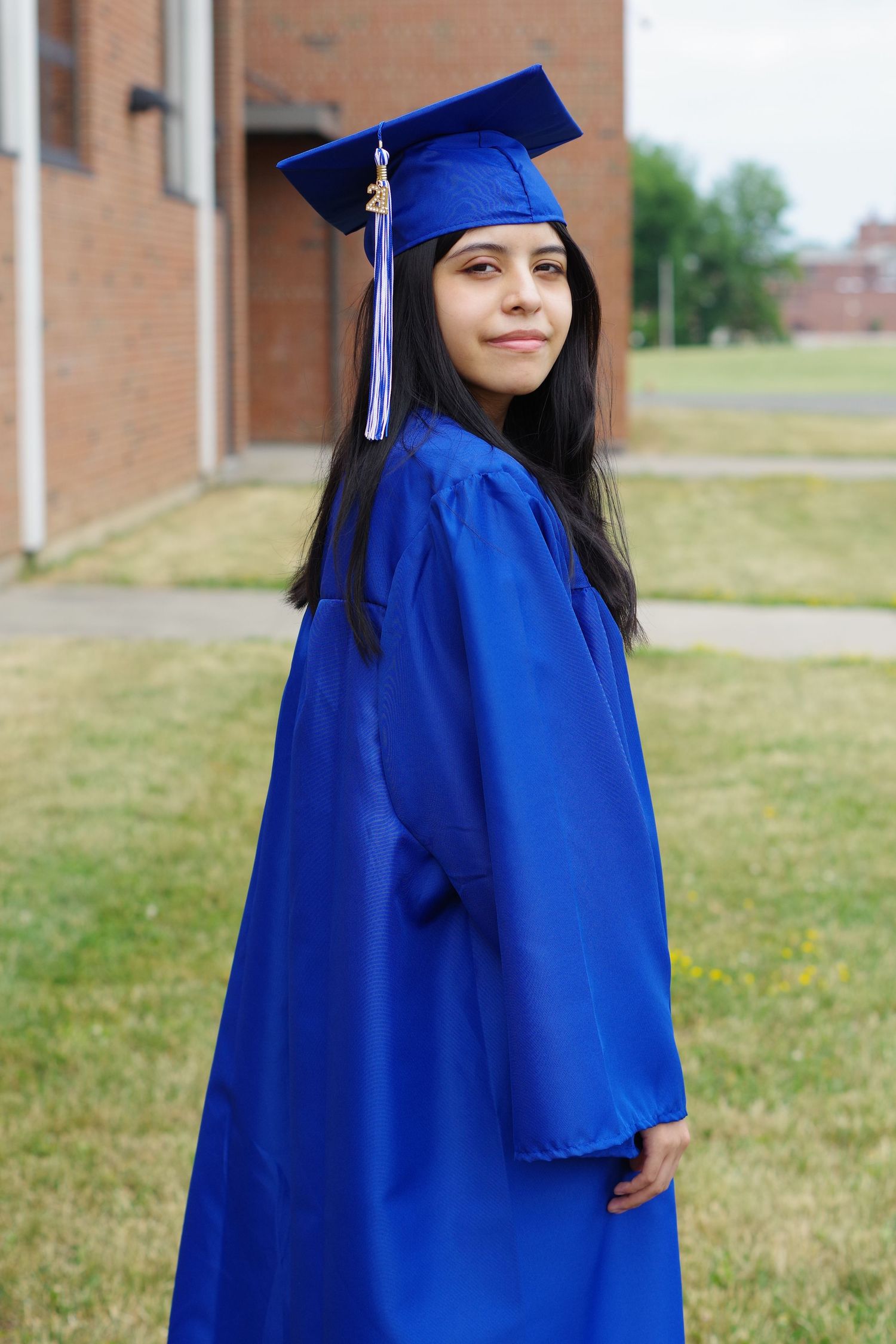 Graduate in vibrant blue academic regalia poses outdoors near school building.