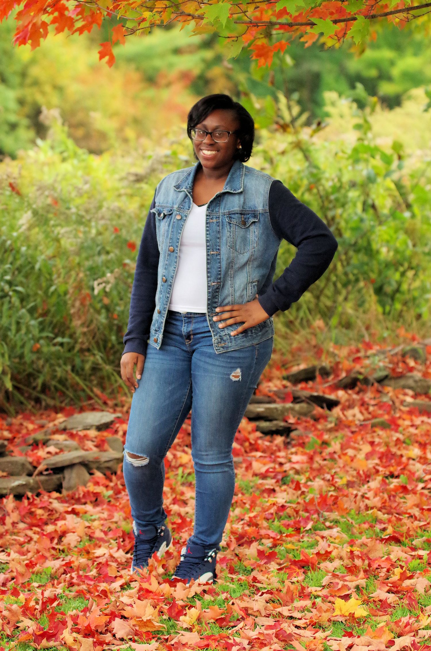 Casual fall portrait with denim jacket against backdrop of autumn leaves.