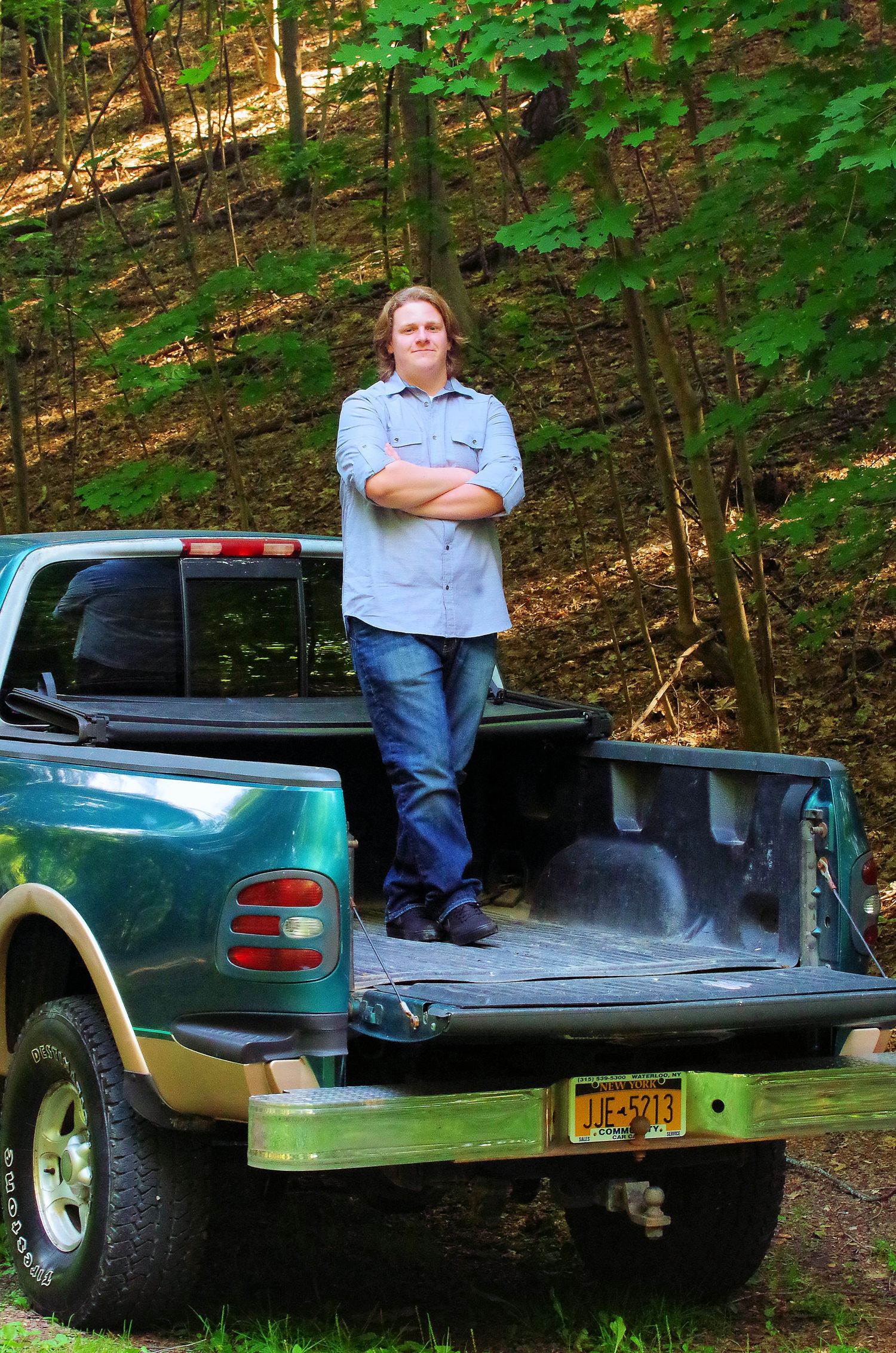 Person sitting on the bed of a green pickup truck in a wooded setting.