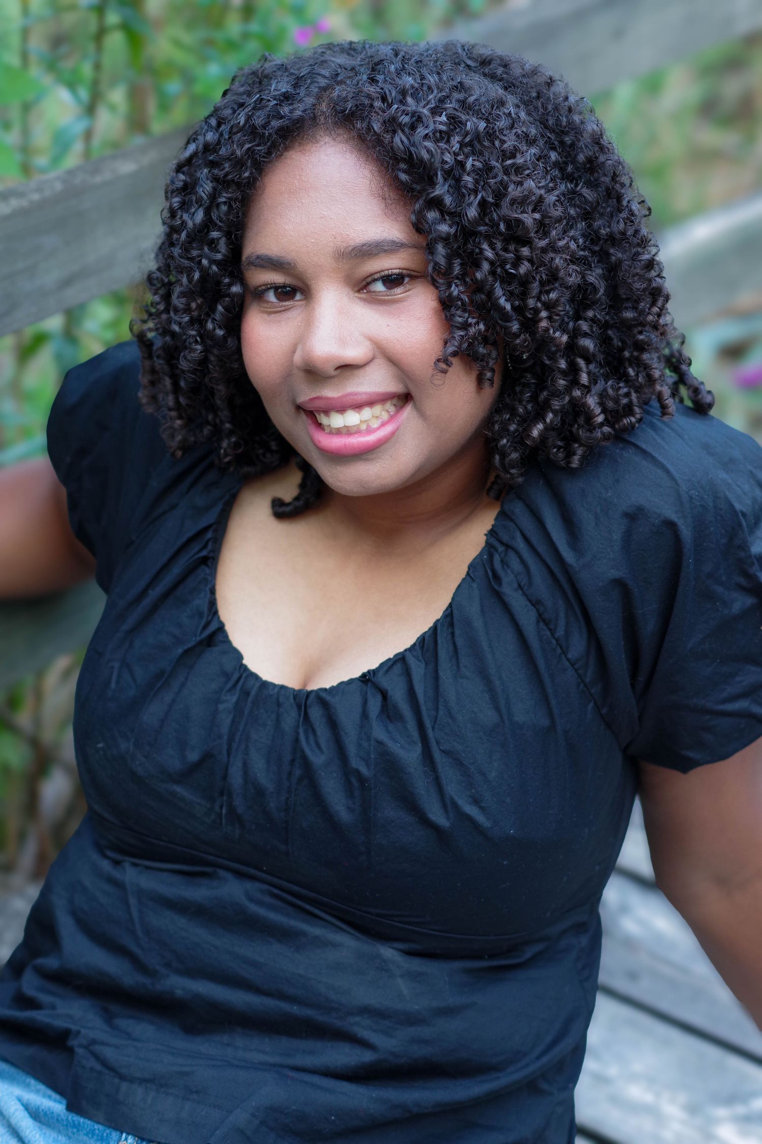 Person with curly hair wearing black puff sleeve top poses against natural outdoor background.