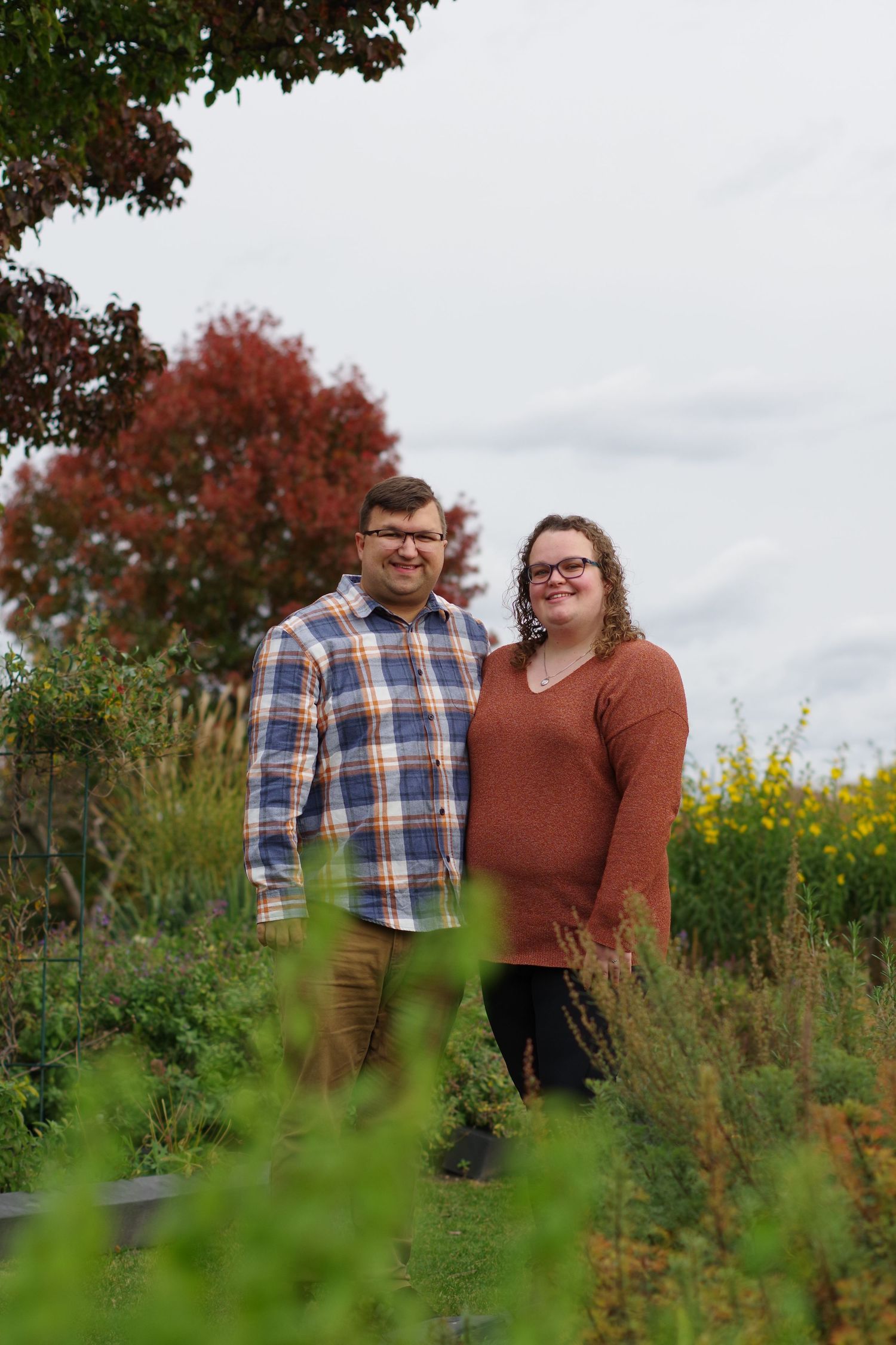 Couple standing together in natural garden setting with red maple tree in background.