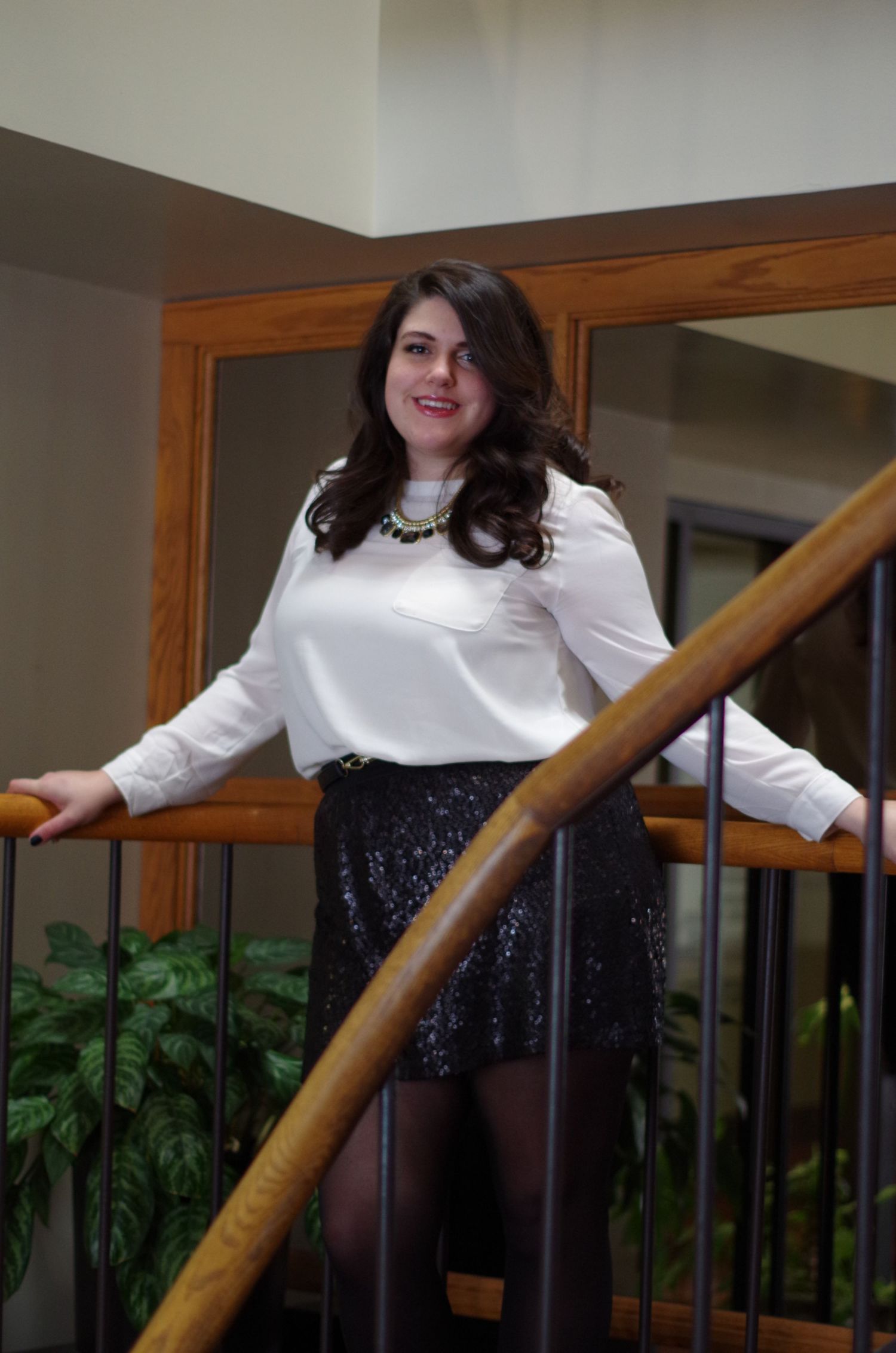 A person poses on stairs wearing a white blouse and sequined skirt.