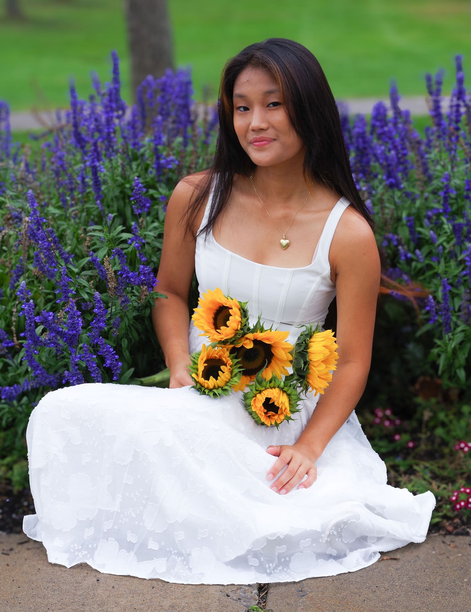 White sundress and sunflowers create beautiful contrast against purple flowers in garden setting.