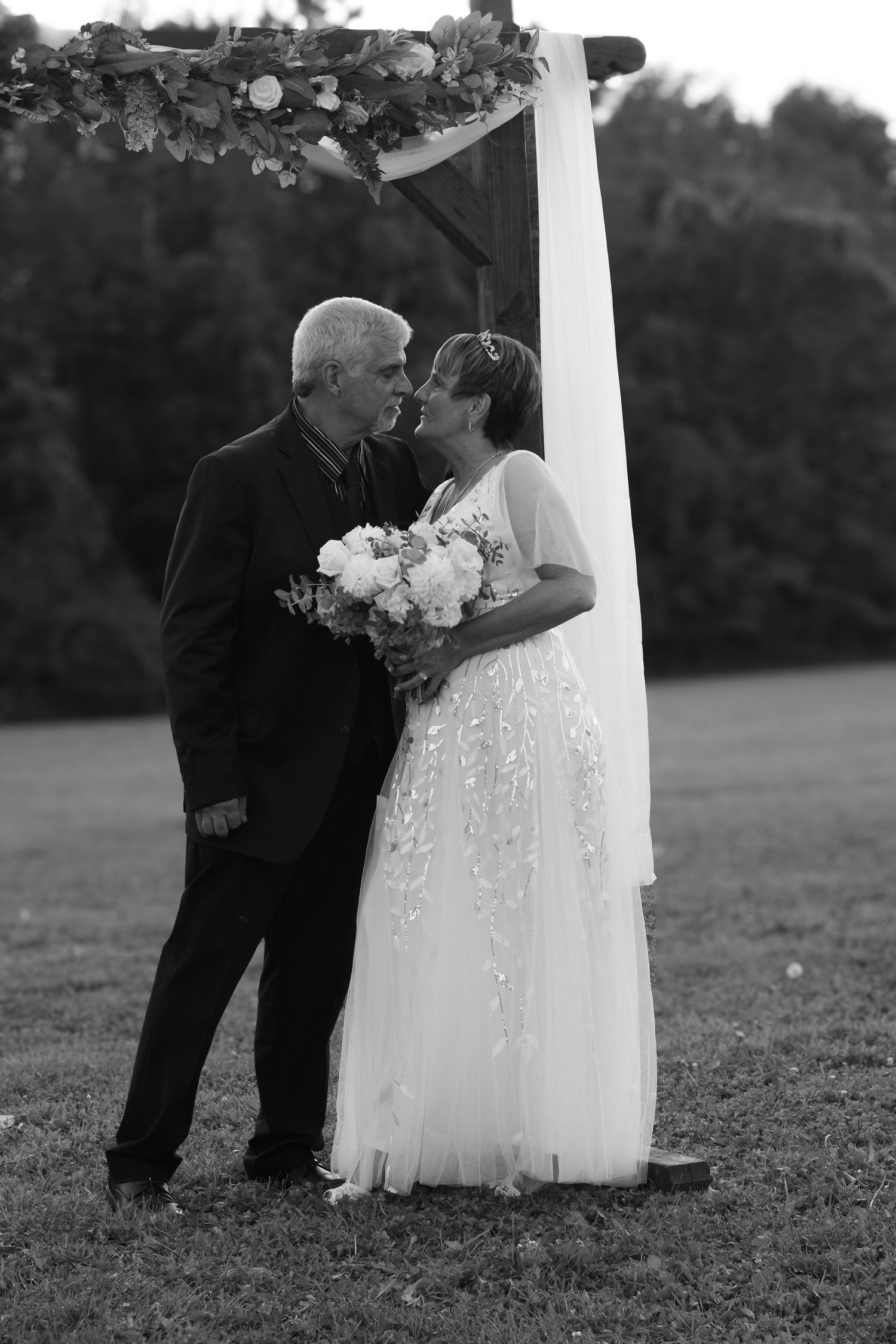 A tender black and white wedding moment captured under a floral arch outdoors.