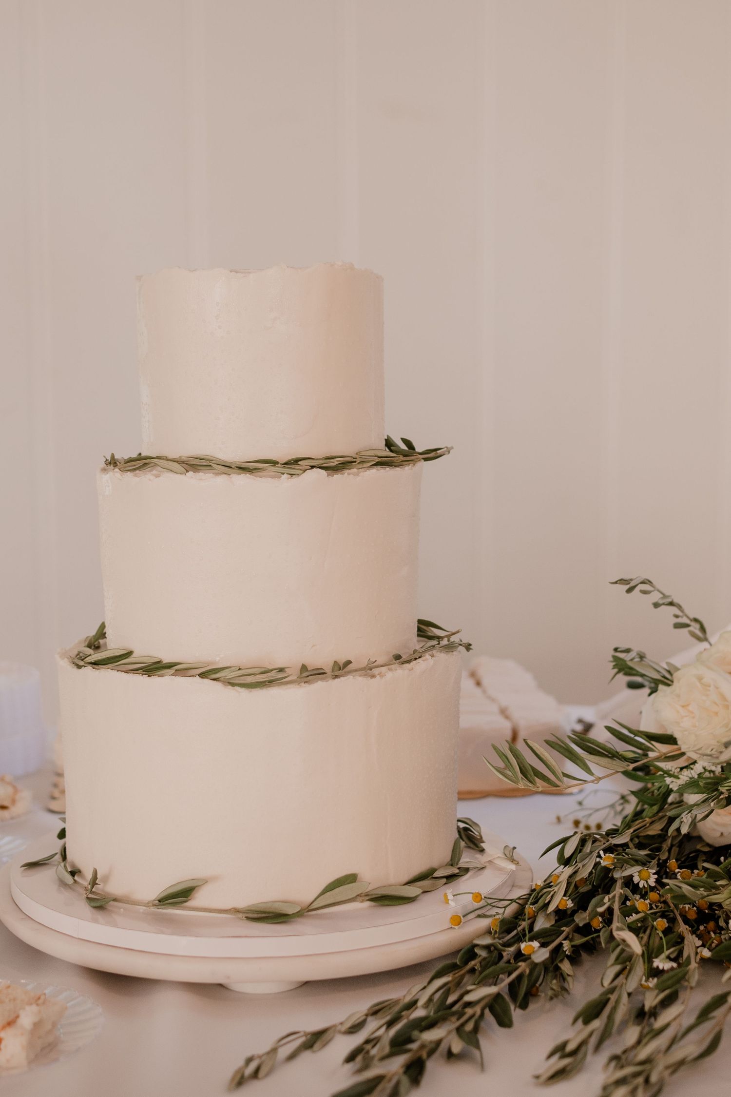 Elegant three-tier white wedding cake decorated with delicate greenery garlands.