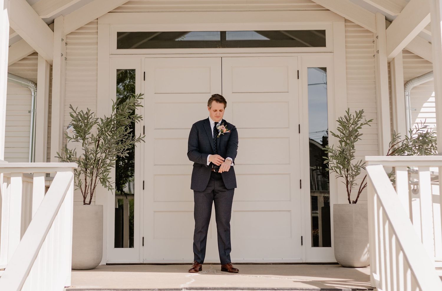 Candid portrait of groom outside of historic Bishop Arts venue finishing his suit details before first look
