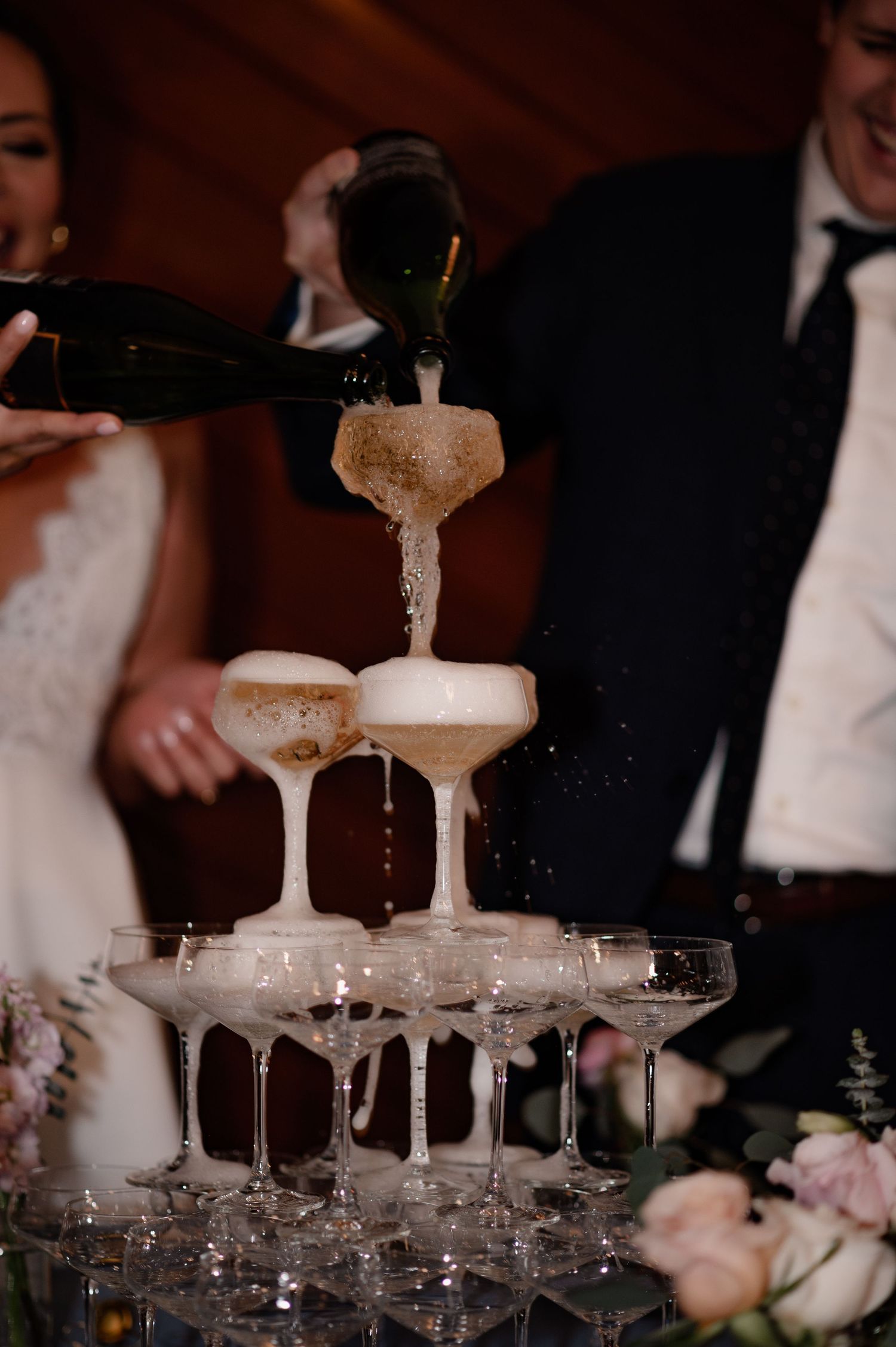 Champagne tower being poured at an elegant wedding reception with crystal coupe glasses stacked in layers