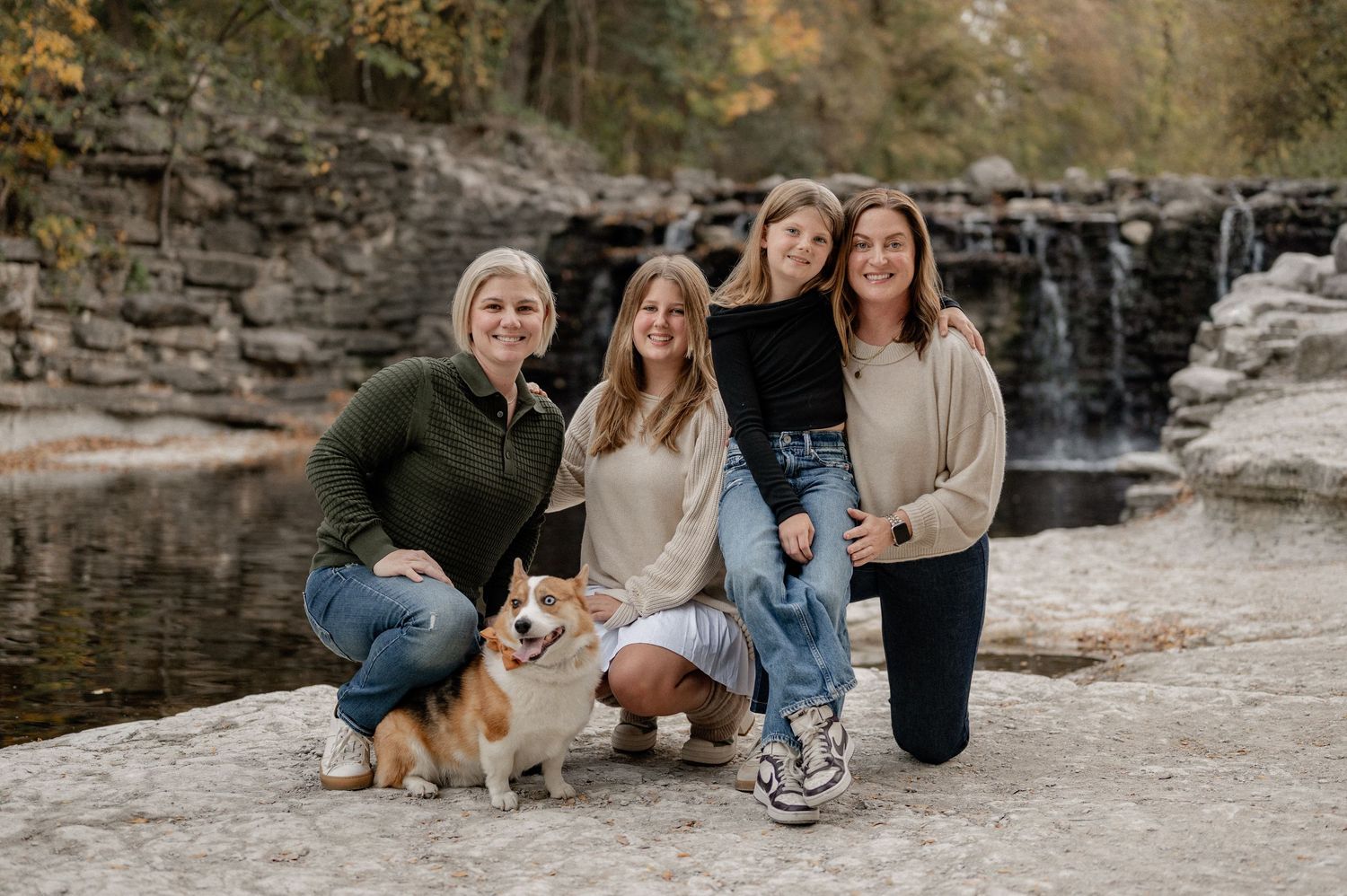 Family and their dog casually posing in front of a running waterfall in Prairie Creek Park in Richardson TX for a fall family photo session