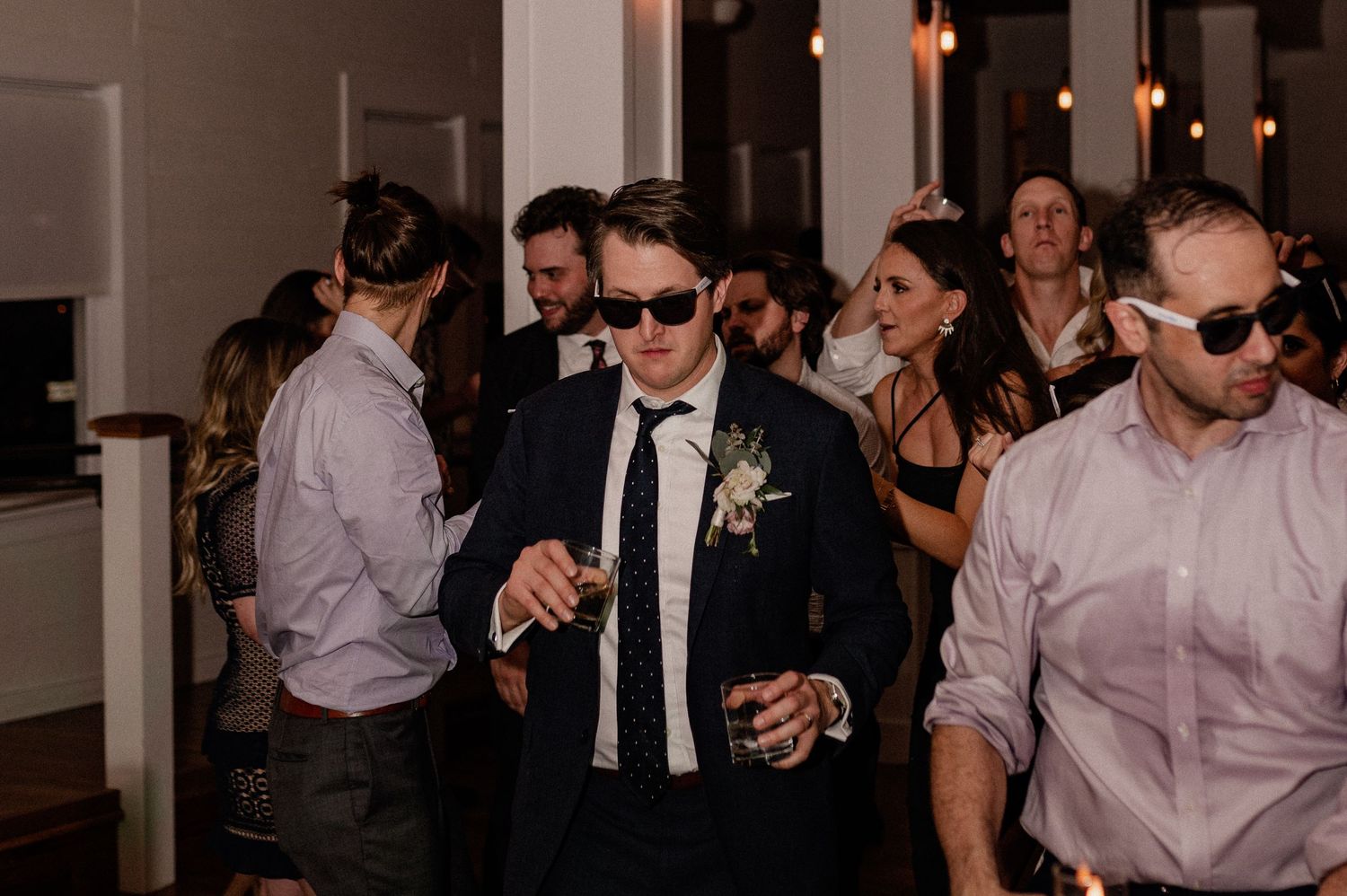 Wedding groom and guests enjoying themselves on the dance floor wearing sunglasses and formal attire.