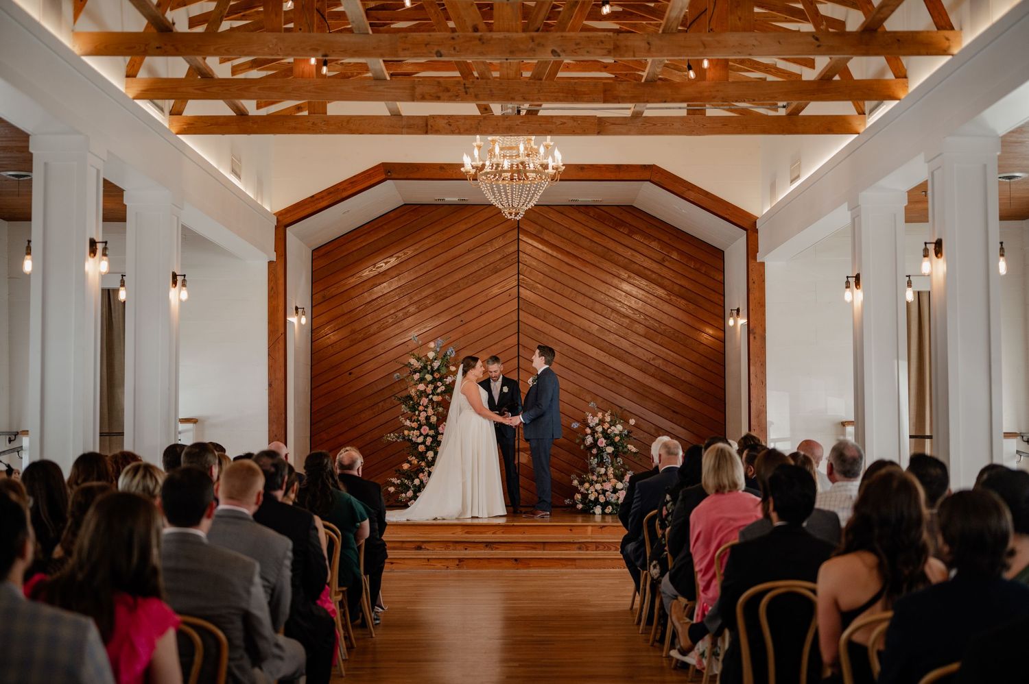 Vintage wedding venue interior with exposed wooden beams and chandeliers during Spring wedding ceremony